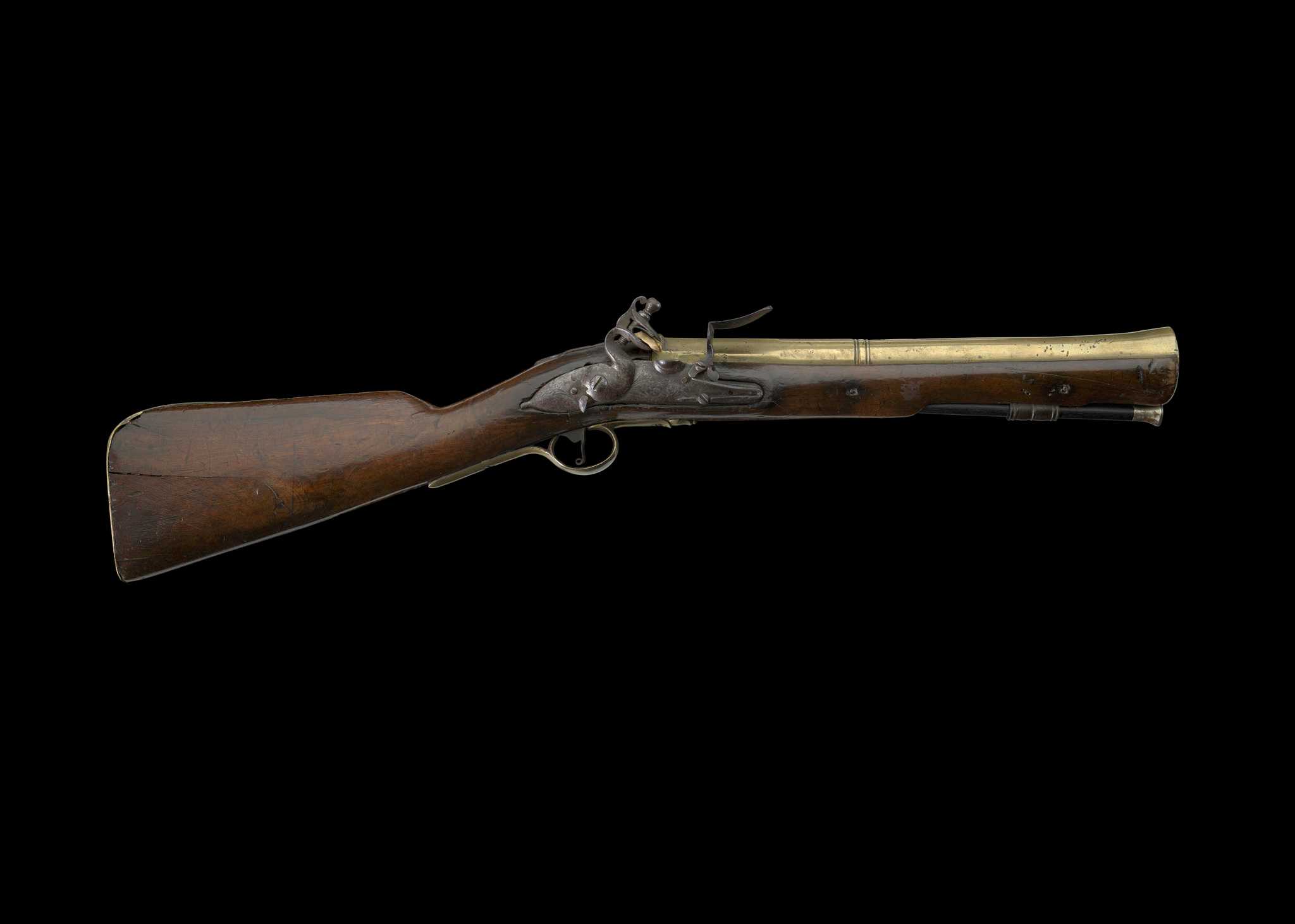 A brass-barreled blunderbuss maded of dark walnut stock and a brass breech is on displayed against a black background.