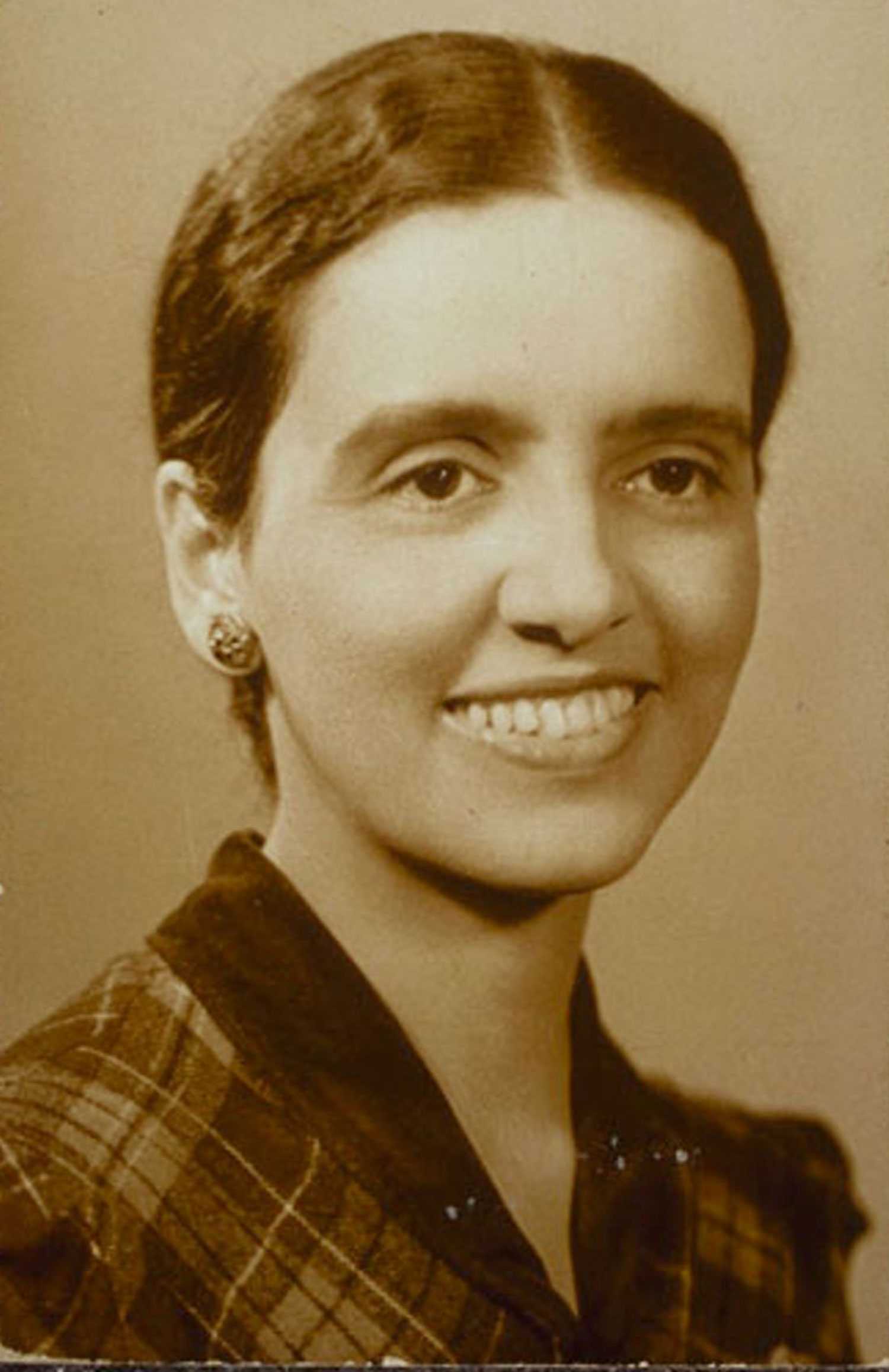 Portrait of a smiling woman with hair pulled back, wearing a checkered top.