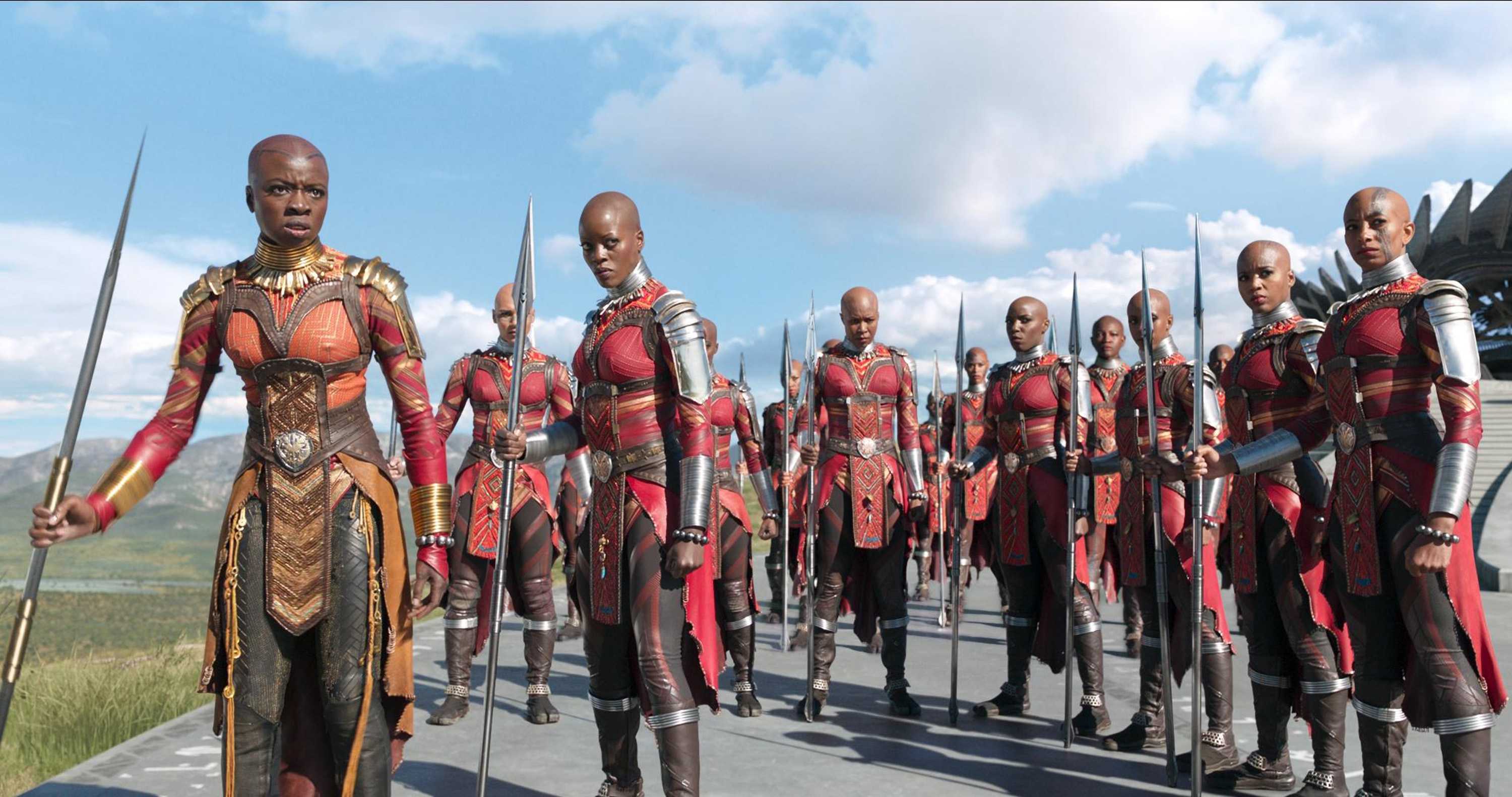 Danai Gurira and Florence Kasumba as leaders of the Dora Malaje ready to fight. The army is dressed in battle gear, looking away at their opponents.