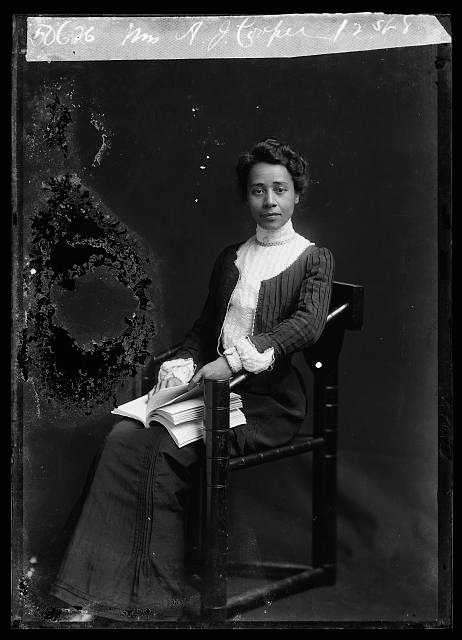 A black and white portrait photograph of a Anna Julia Cooper seated in chair with a book in her lap.
