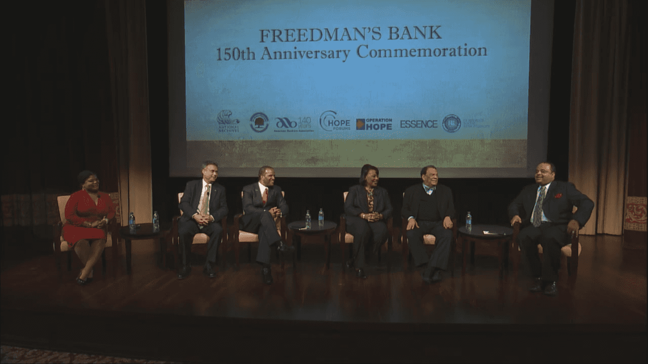 6 people sit on a panel in front of a projected screen that says Freedmans Bank 150th Anniversary Celebration