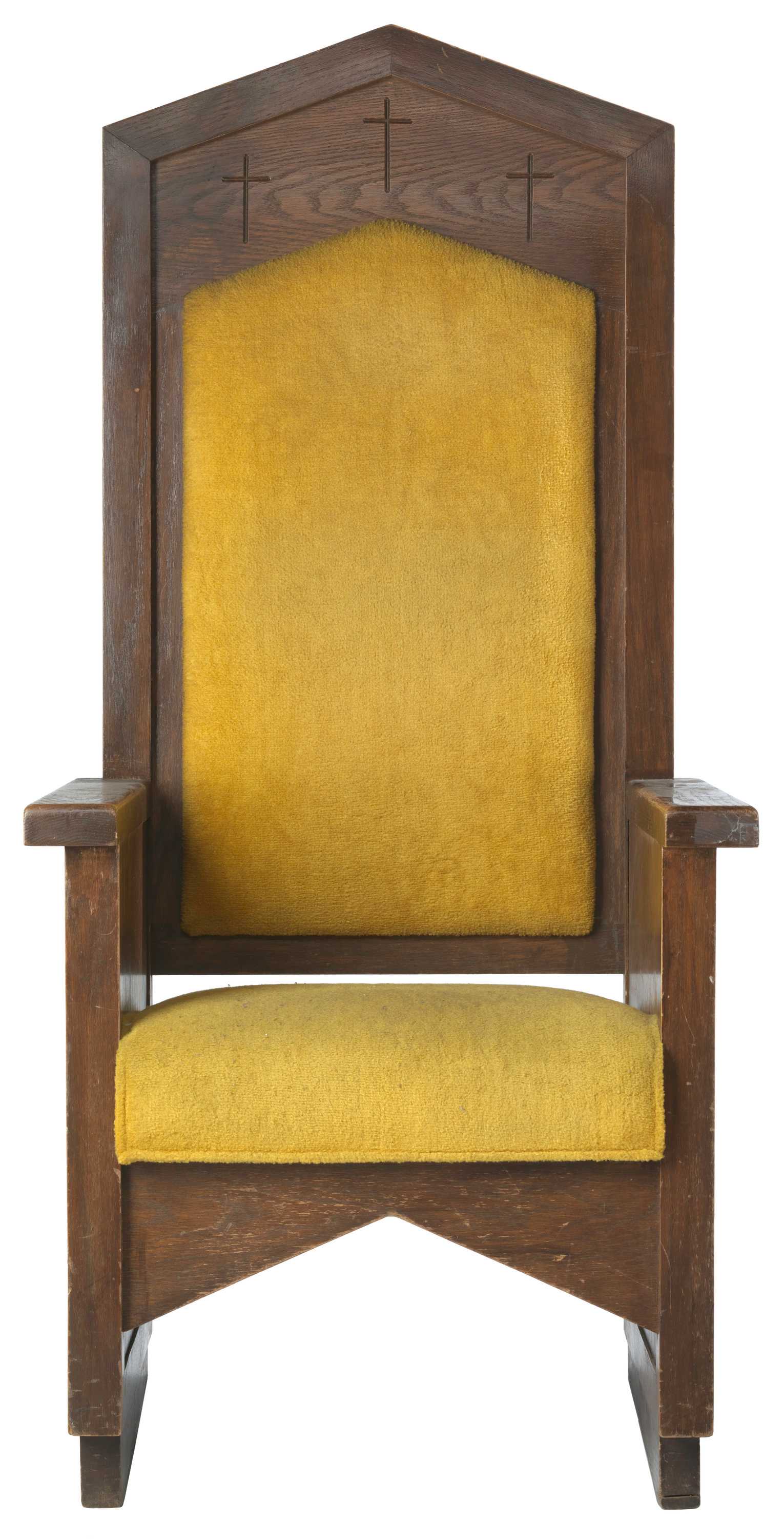 A chair made from dark brown wood featuring yellow back and seat cushions. Three crosses are engraved at the top of the chair. The back of the chair is consistent in design with the church archway, podium, and windows.