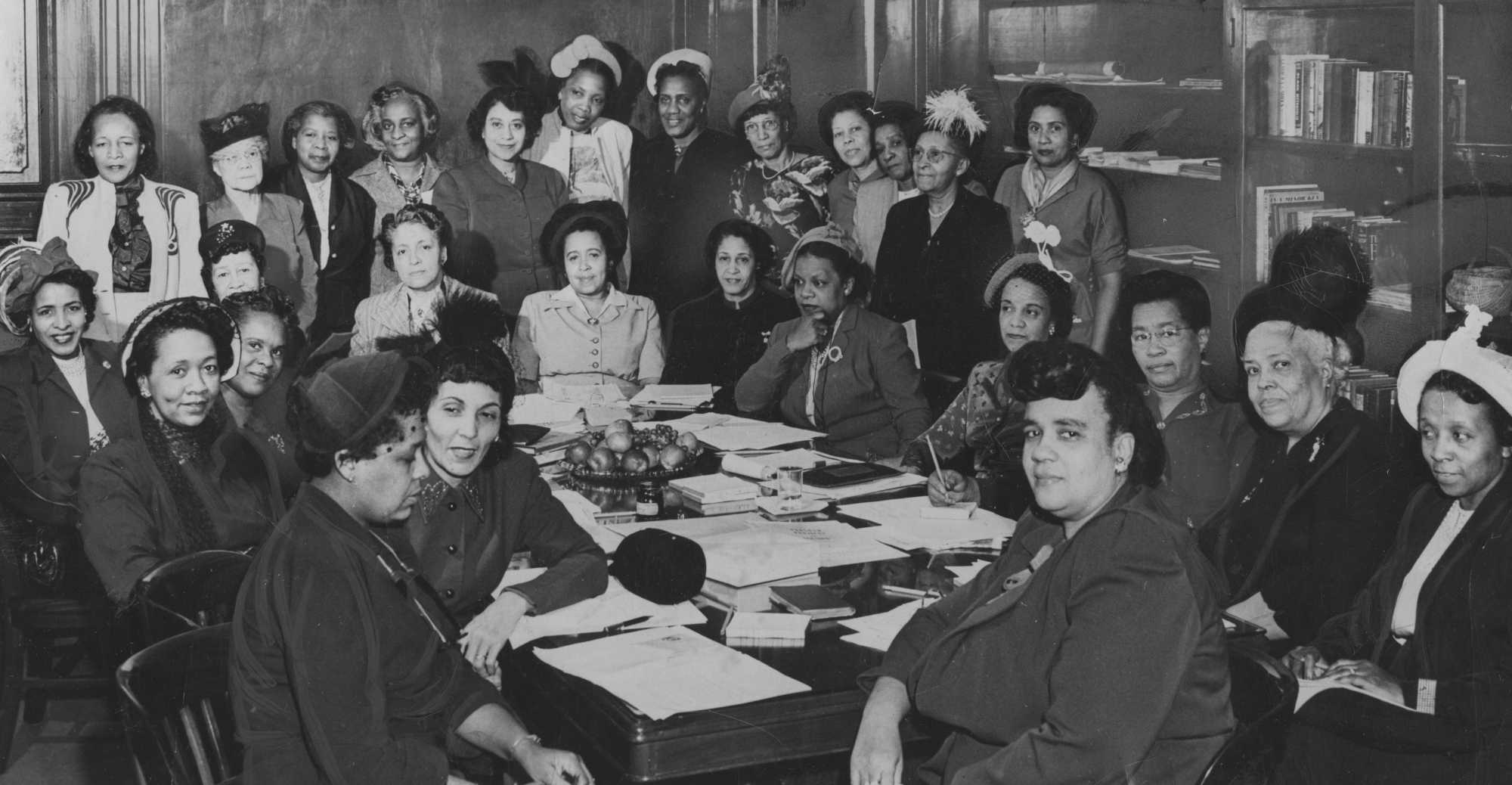 Officers and members attend an executive session, and take a picture seated around the table, with documents and books in a library