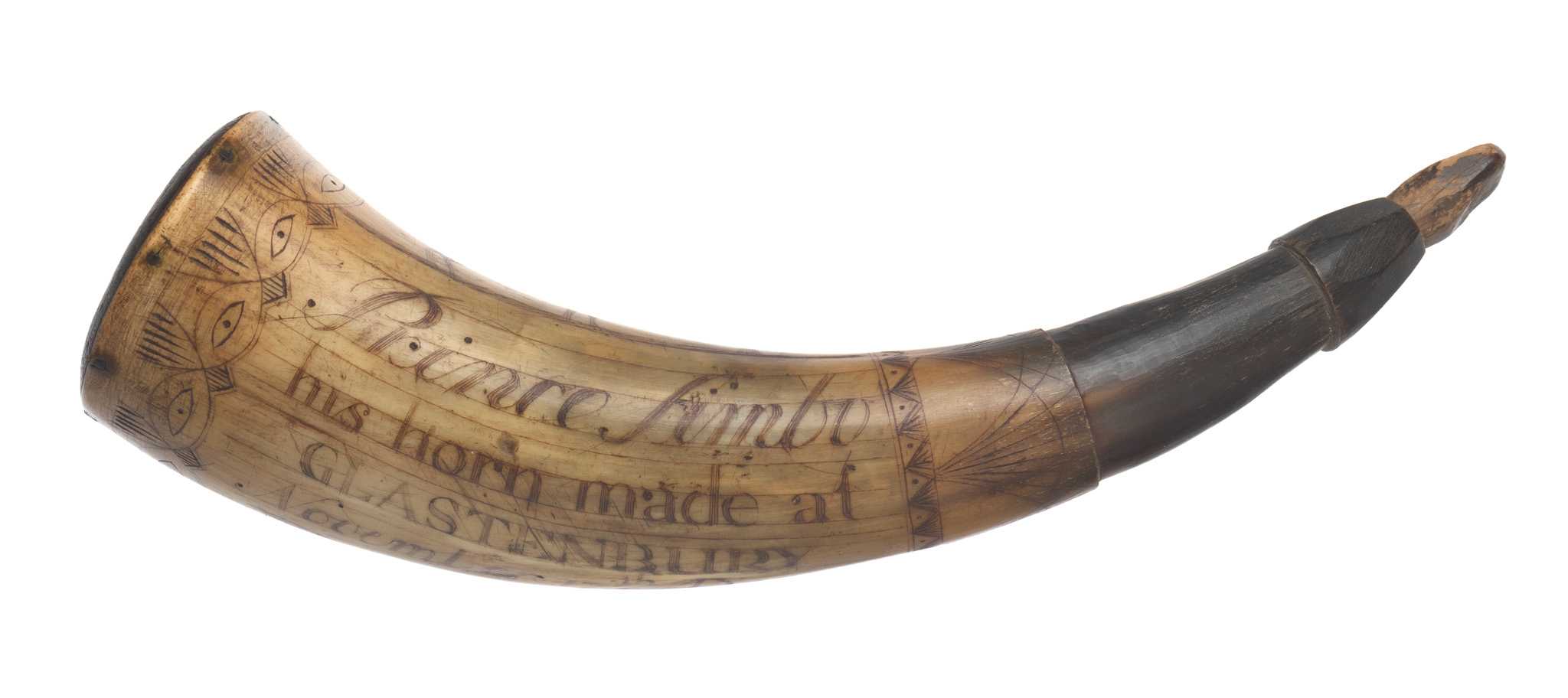 An engraved powder horn with stopper. The ox horn is carved with images of a dove carrying a banner reading "LIBERTY," a deer, the sun with a face, and a pine tree. An intricate design featuring eyes encircles the outer edge of the horn. The name Prince Simbo and the date November 17, 1777 are also engraved on the horn.