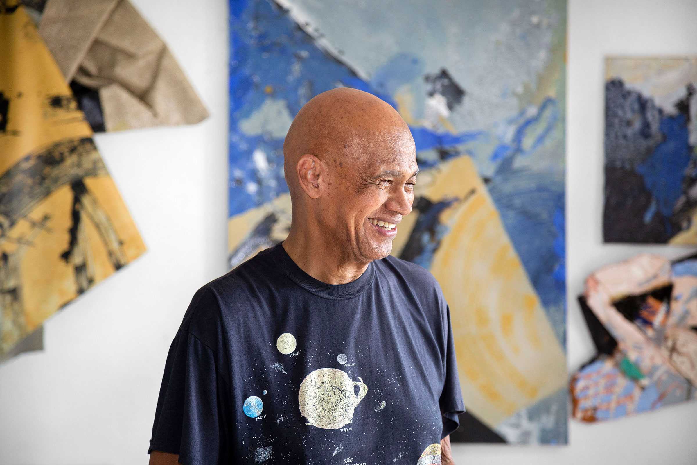 A man smiling in front of abstract artwork with colorful geometric shapes.