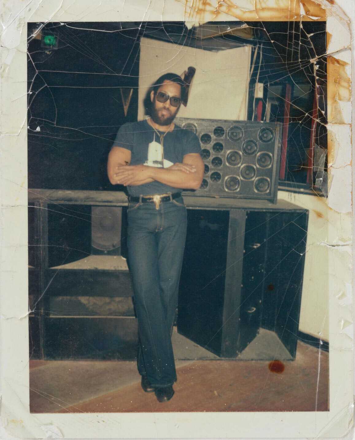Color photograph of man standing in front of sound system with arms crossed