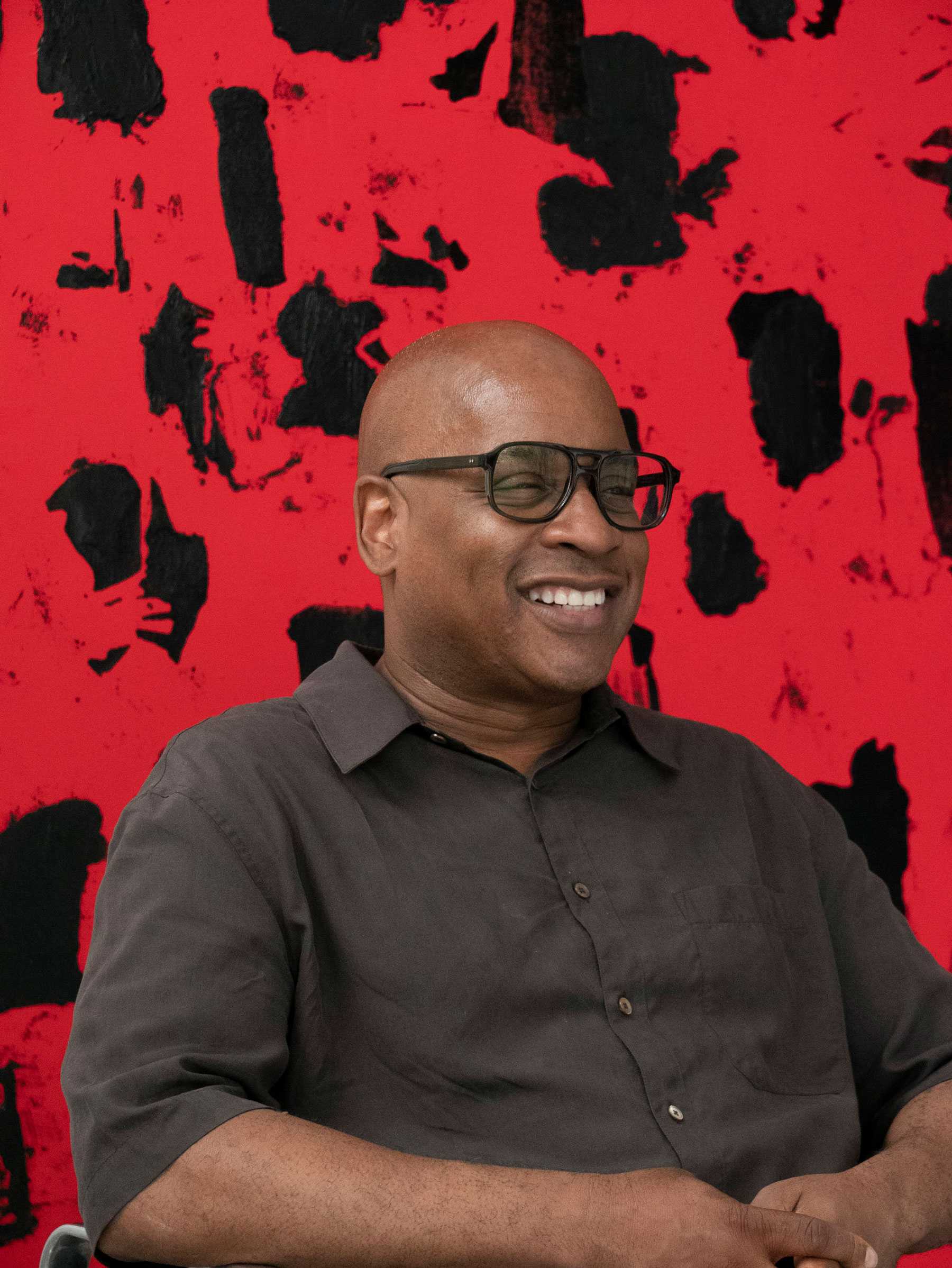 Man smiling with glasses in front of a red and black abstract background.