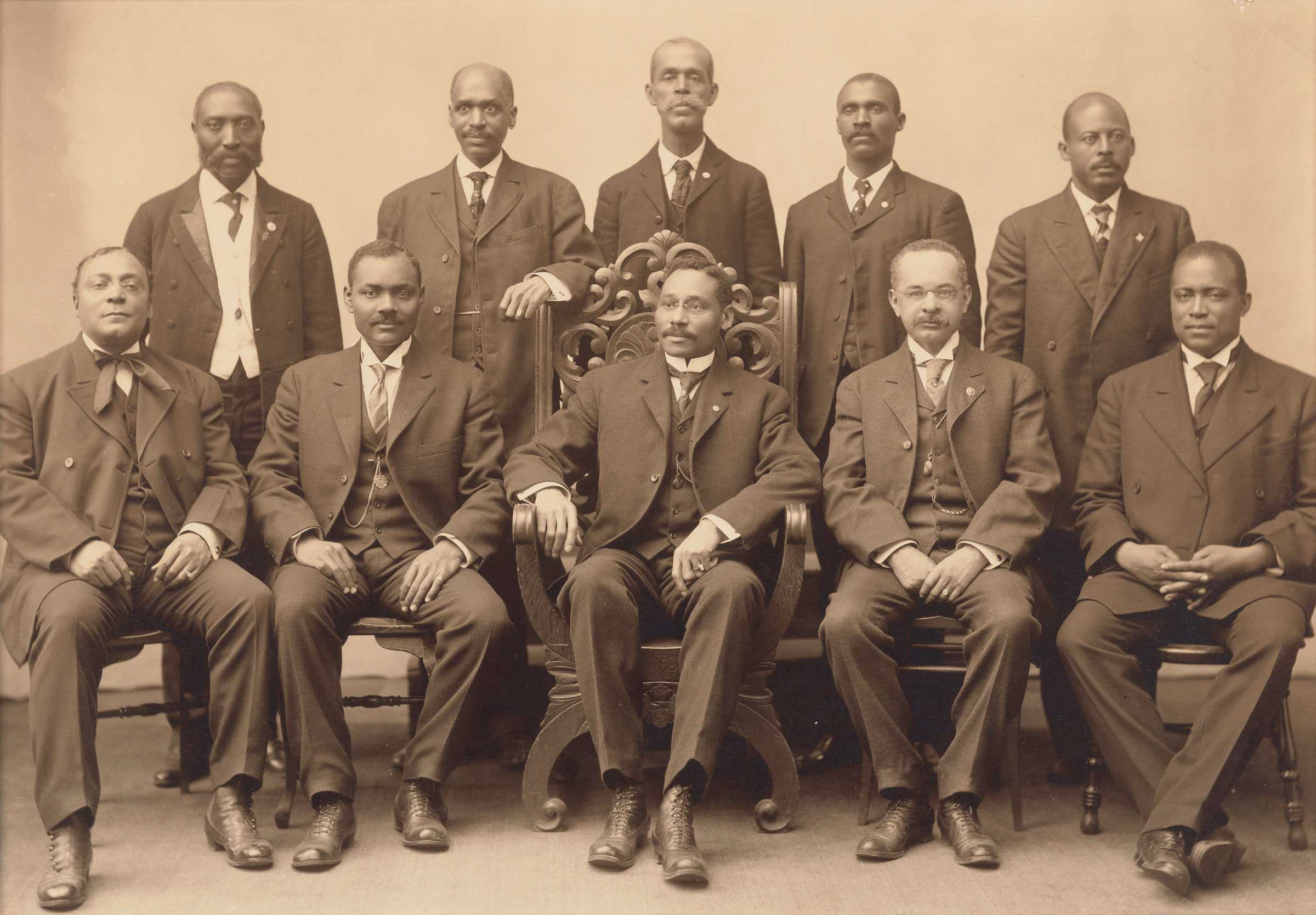 A sepia toned portrait of 10 committee members posing for the photo in a studio.