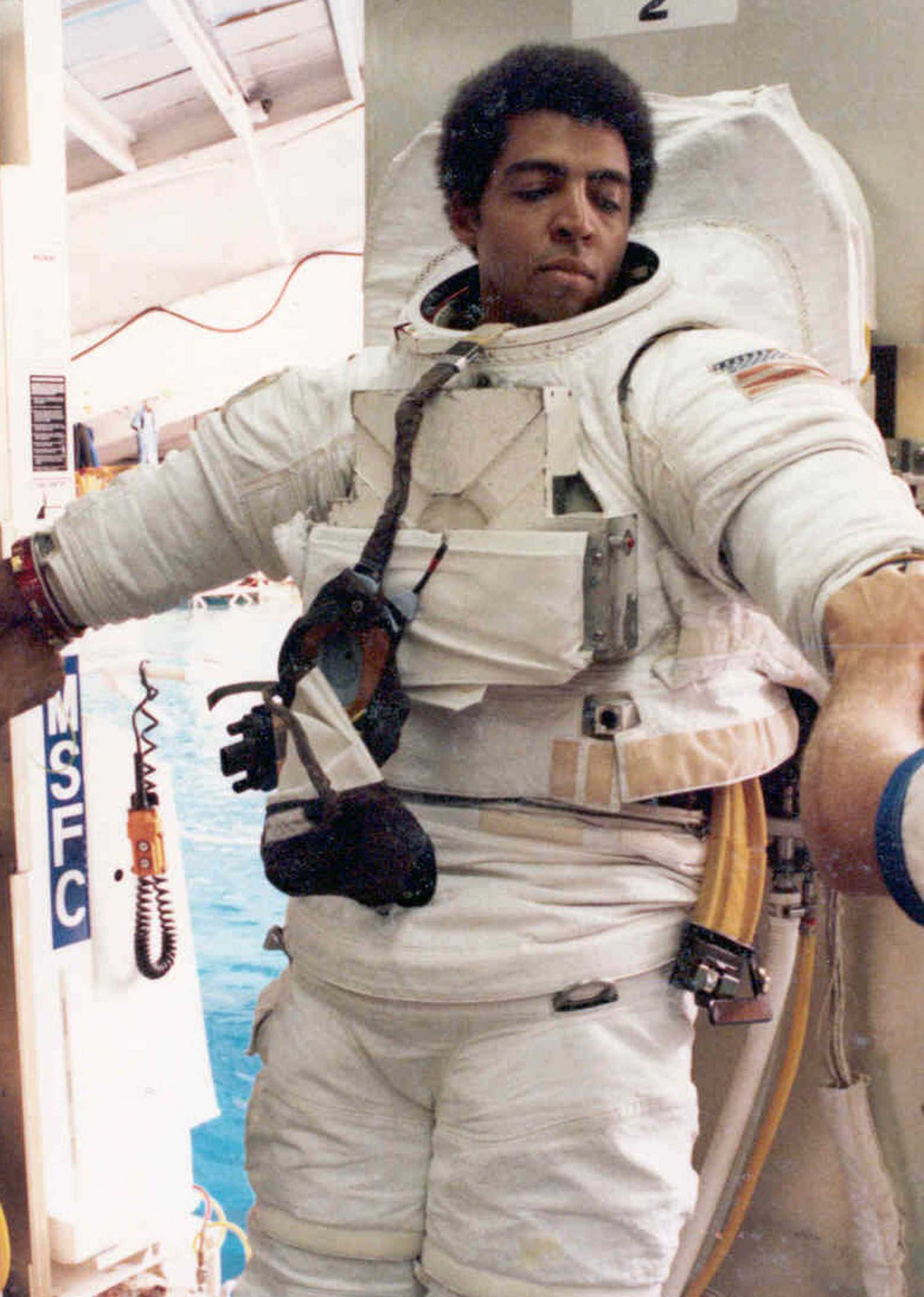 Livingston Holder is getting his white Space suit adjusted as he leans against a wall.