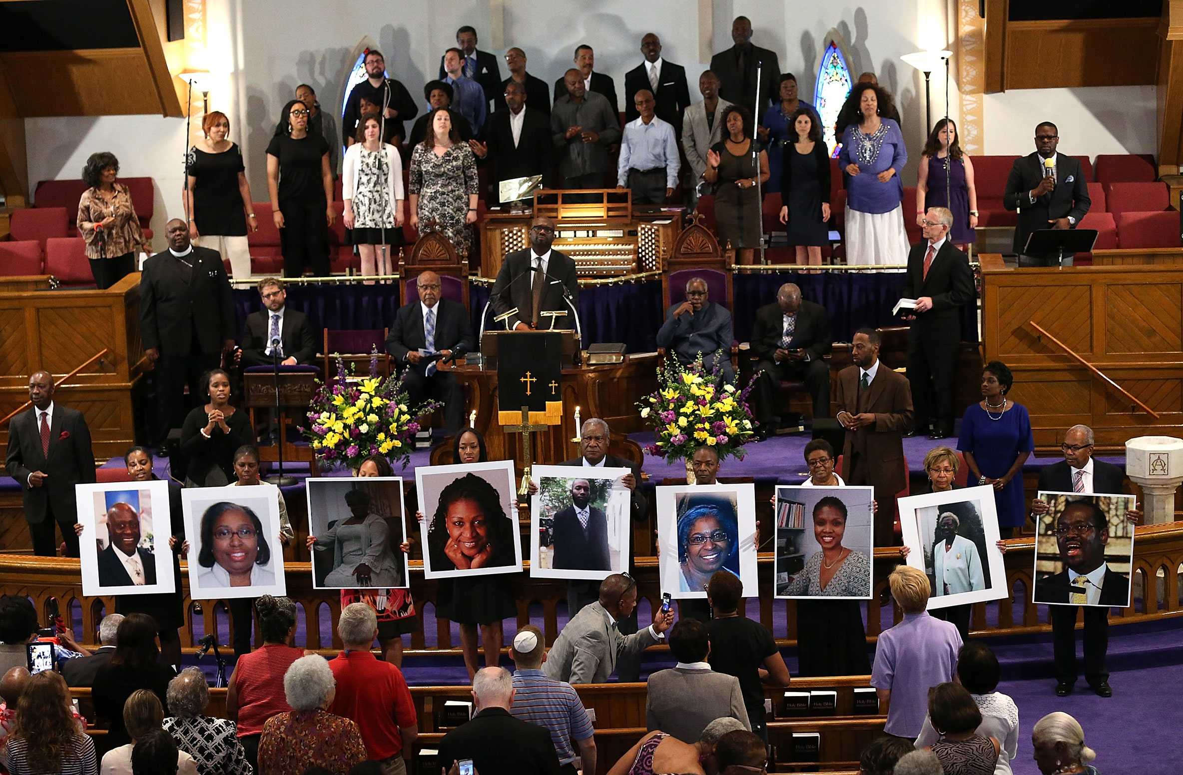 Mourners hold large photos of the victims as choir members and priest stand behind, singing and praying.