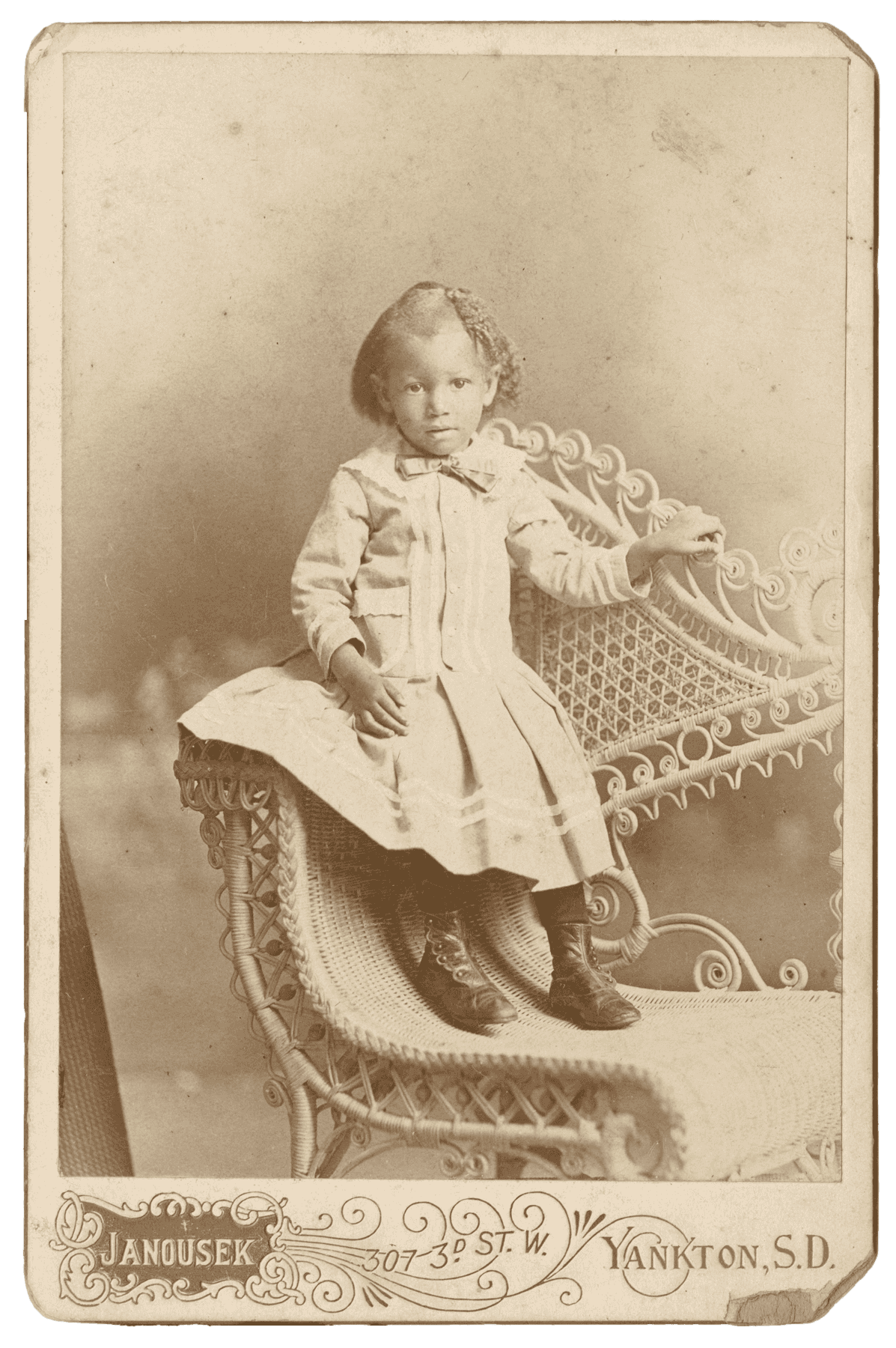 Black and white cabinet card of a girl wearing a dress and boots.