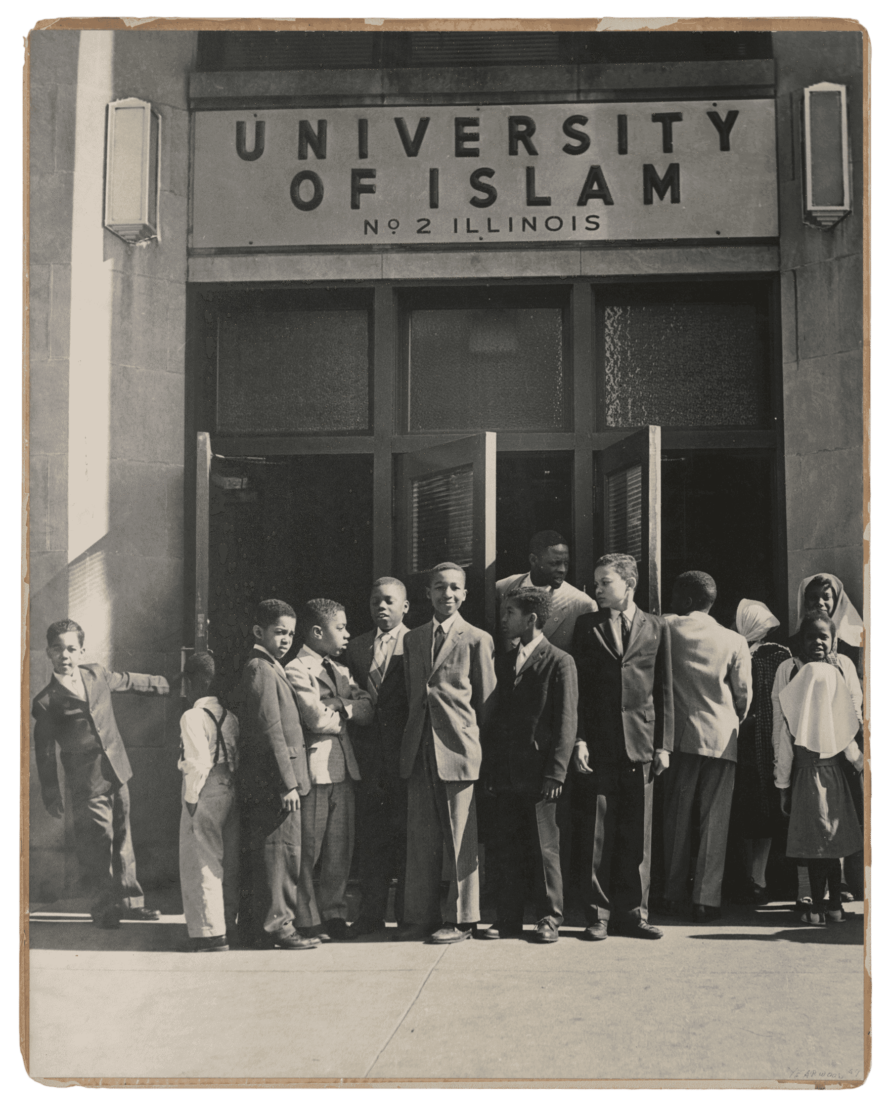 This black and white photograph depicts a group of children standing outside the front doors of the University of Islam.