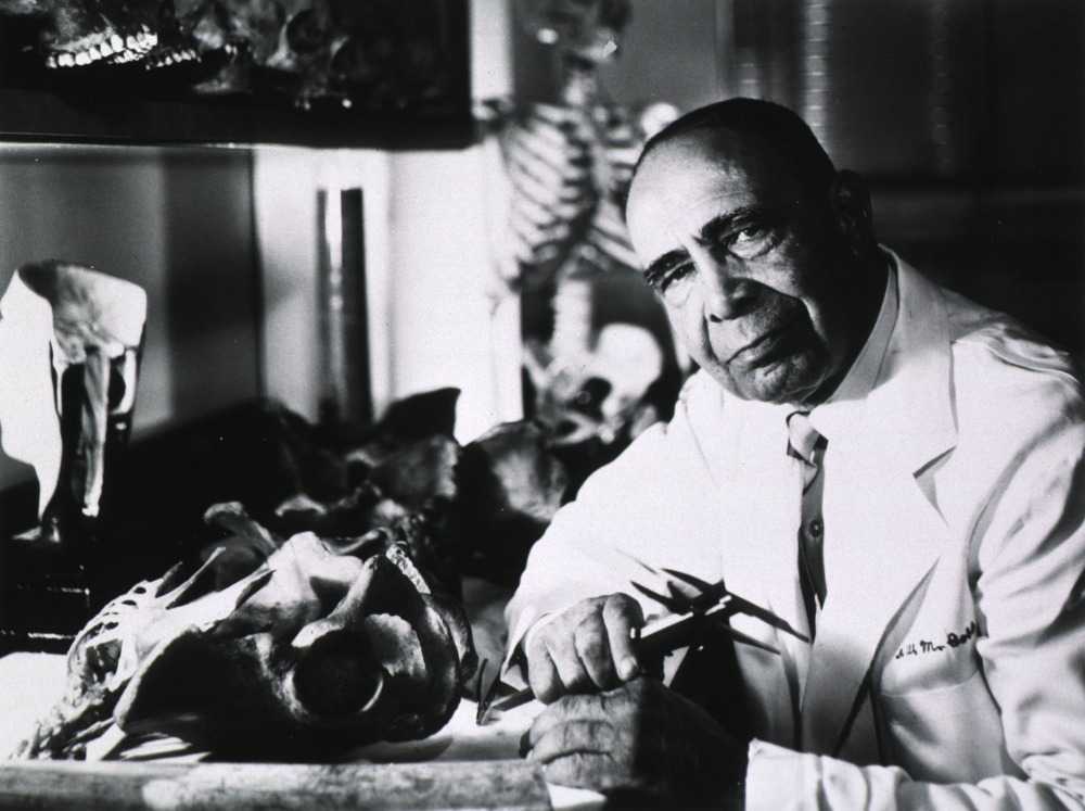 A black and white photograph of Dr. W. Montague Cobb looking at the camera in a lab coat.