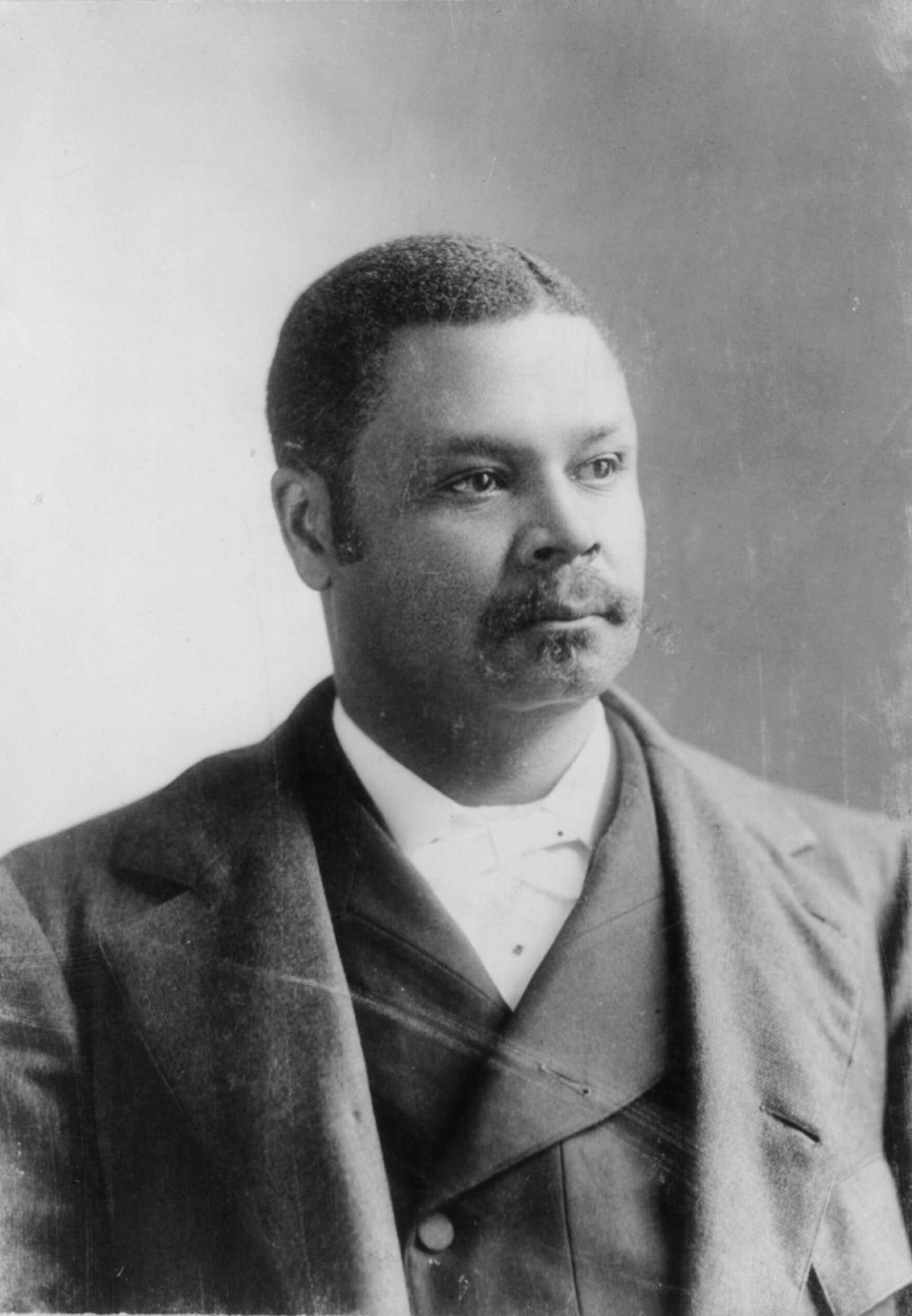 A worn black and white photo of George H. White. He is looking off camera in a suit.