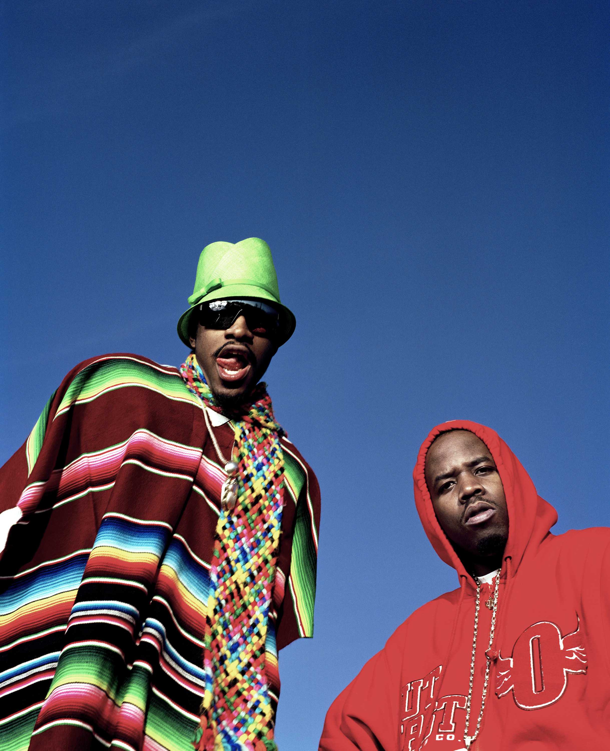 Against a blue sky, André 3000 and Big Boi stand above the camera. Big Boi is dressed in a red hoodie.