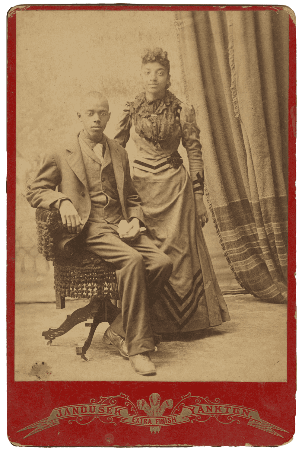 Black and white cabinet card of a man seated with a woman standing next to him.