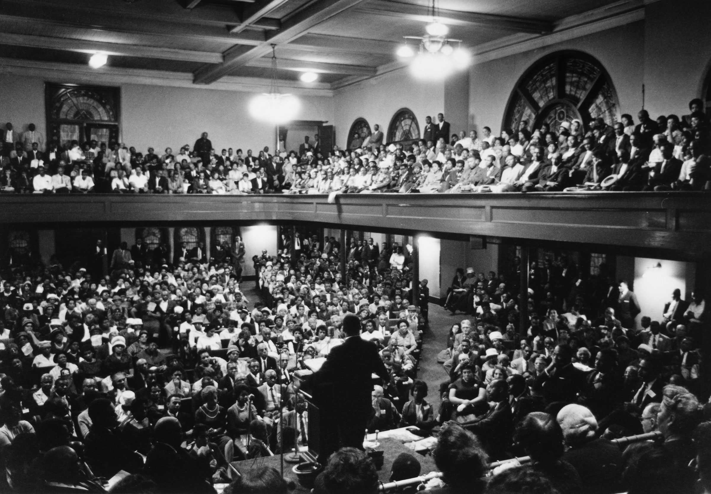 Black and white image of Dr. Martin Luther King Jr. speaking to a large congregation.