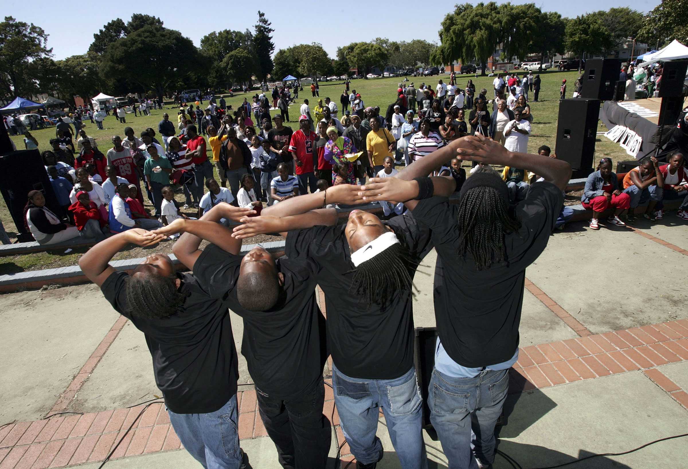 Group of four people performing a coordinated dance in front of a large crowd at an outdoor event.
