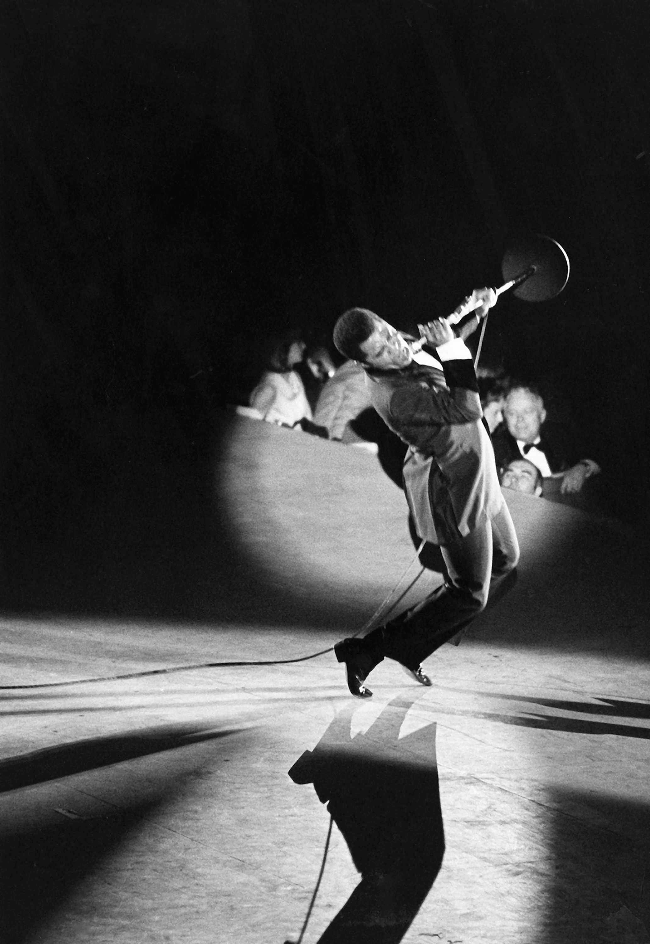 Black and white photograph of James Brown performing on stage with a microphone