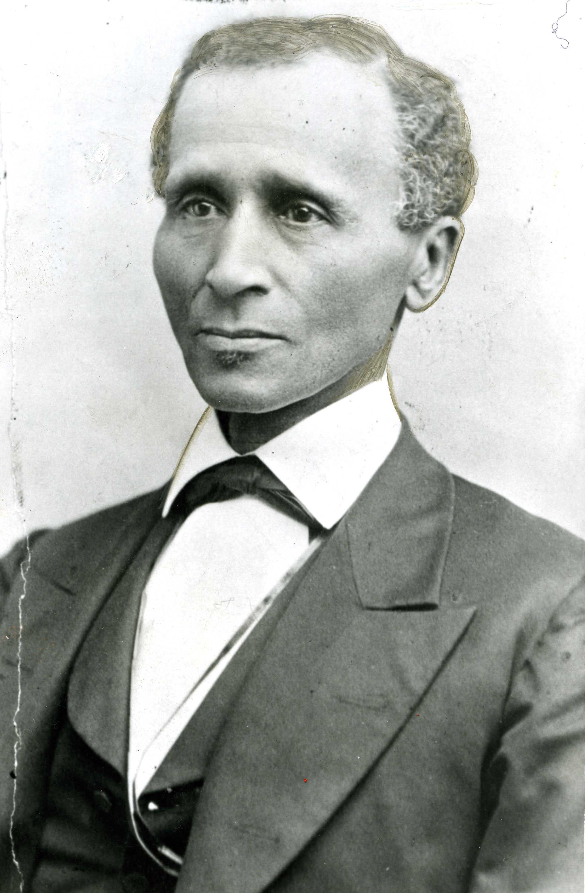 Black-and-white portrait of a man in a suit and bow tie, facing forward, with a neutral expression.