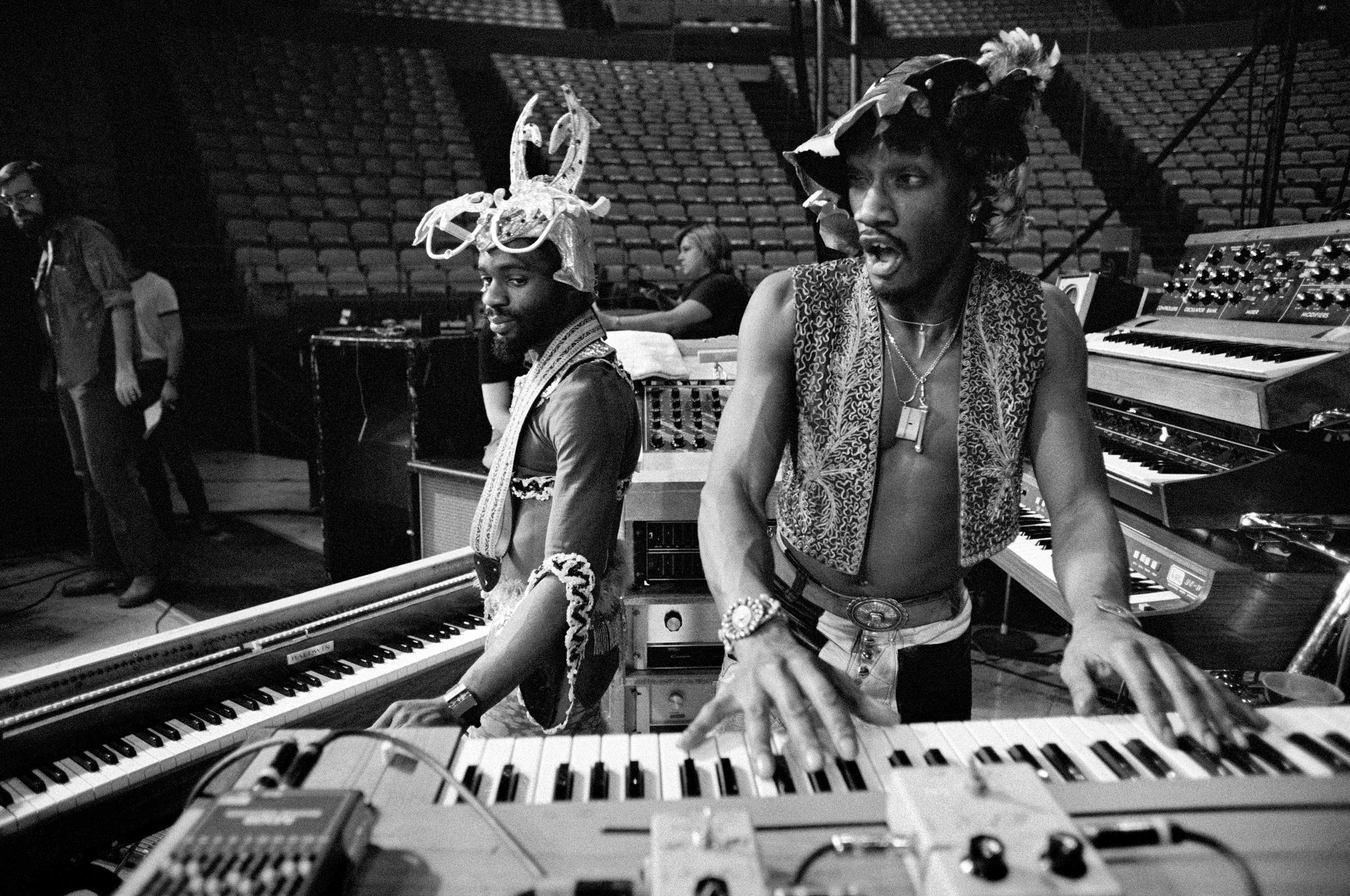 Bernie Worrel is playing the keyboard in a empty stadium while Boogie stands behind him.