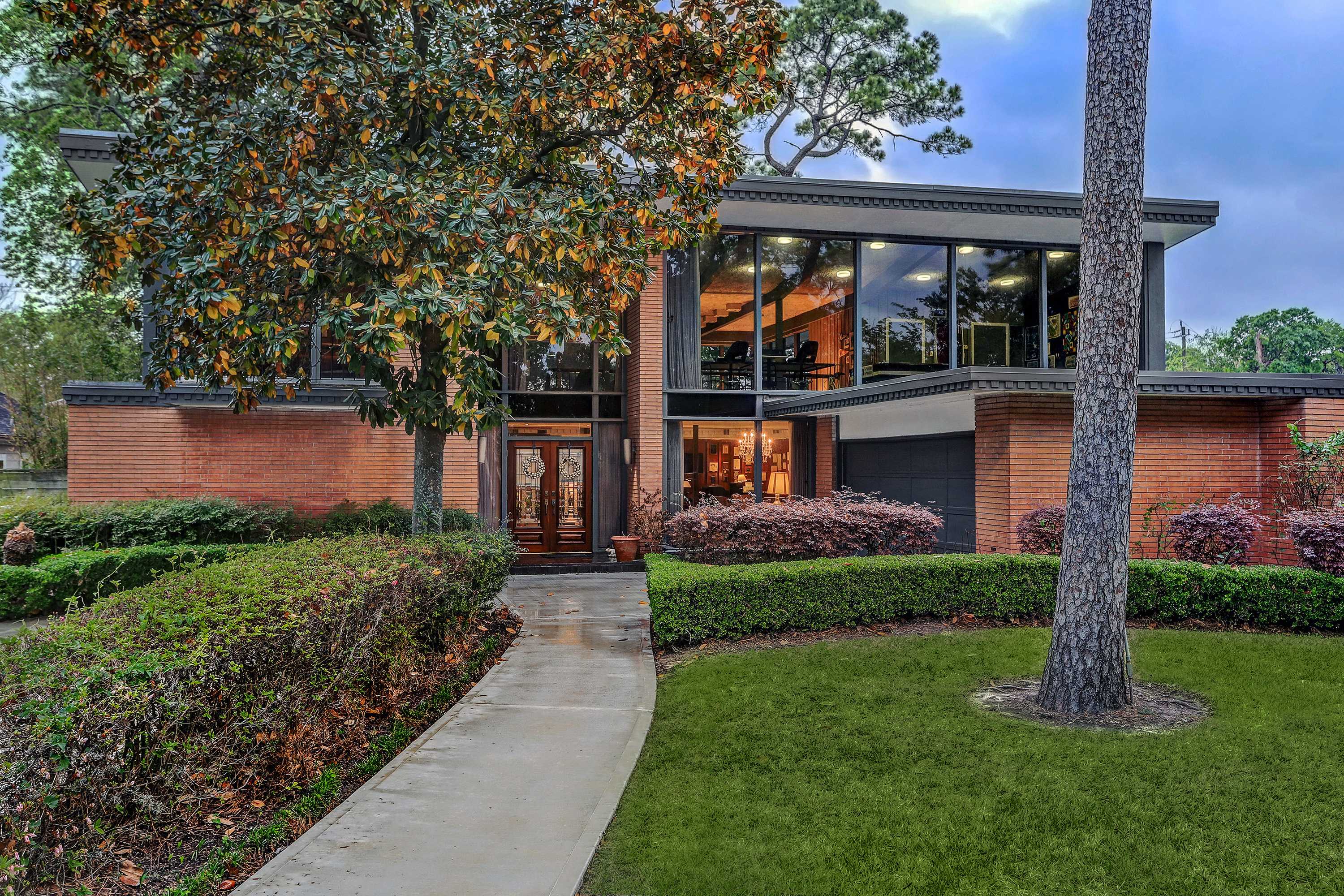 Brick, mid-century modern house that was designed by the architect John Chase.  The house has a second floor with large windows that span the length of the home. .