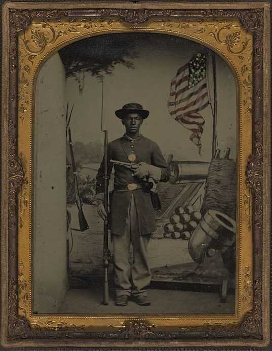 Black solider dressed in Civil War uniform holding a pistol and rifle