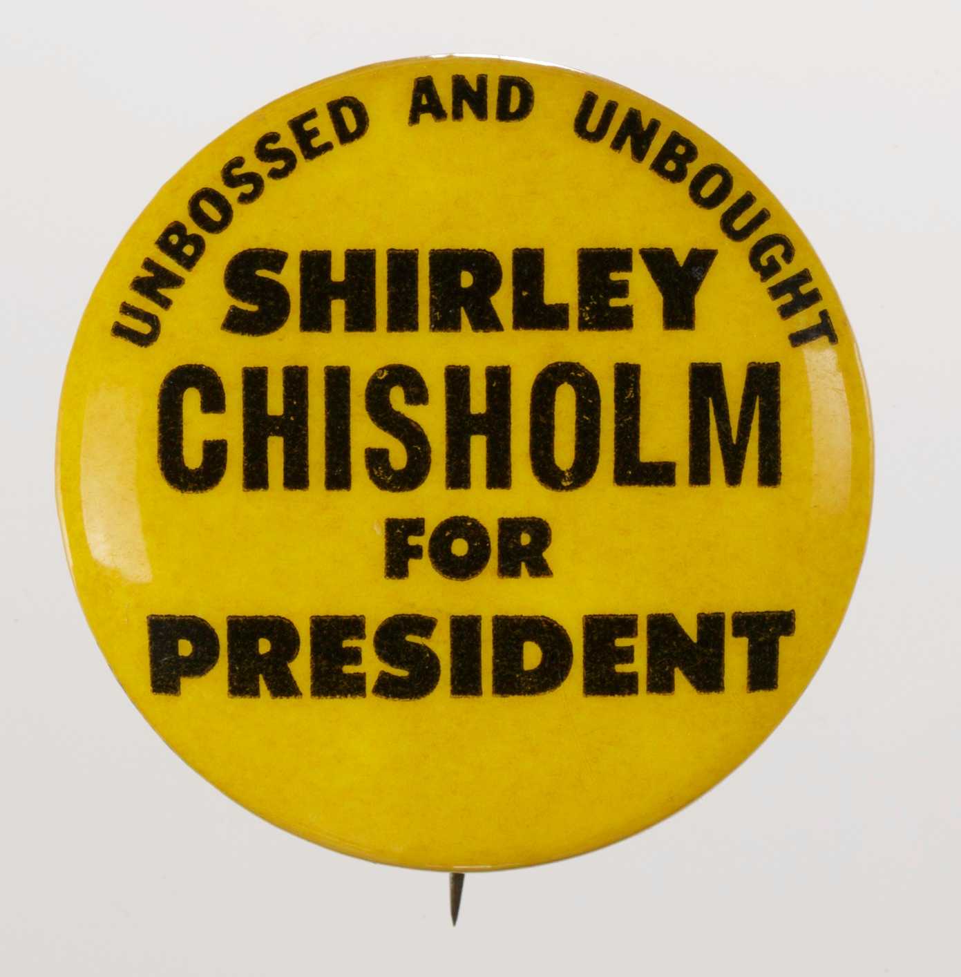 A circular metal pin-back button. It has a yellow background with black type that reads: [UNBOSSED AND UNBOUGHT / SHIRLEY / CHISHOLM / FOR / PRESIDENT]. The fonts vary in size. Black type, around the edge of the pin reads:  [LARRY FOX ASSOC. P.O. BOX 581 HEMPSTEAD NEW YORK]. The back of the button is silver in color, has a single pin without a clasp and an engraving.