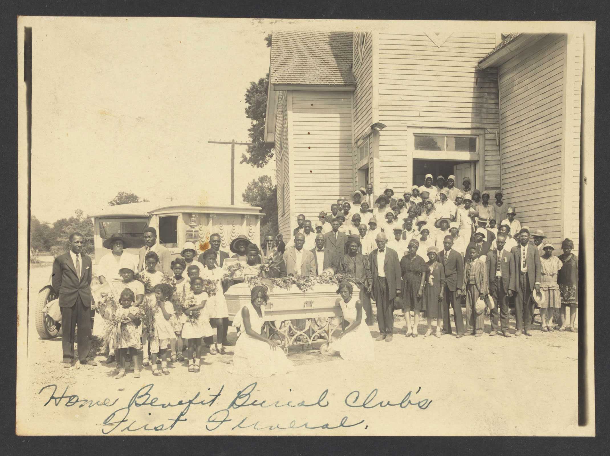 A large group of African Americans taking a photo around a casket for the first funeral in Earle, Arkansas
