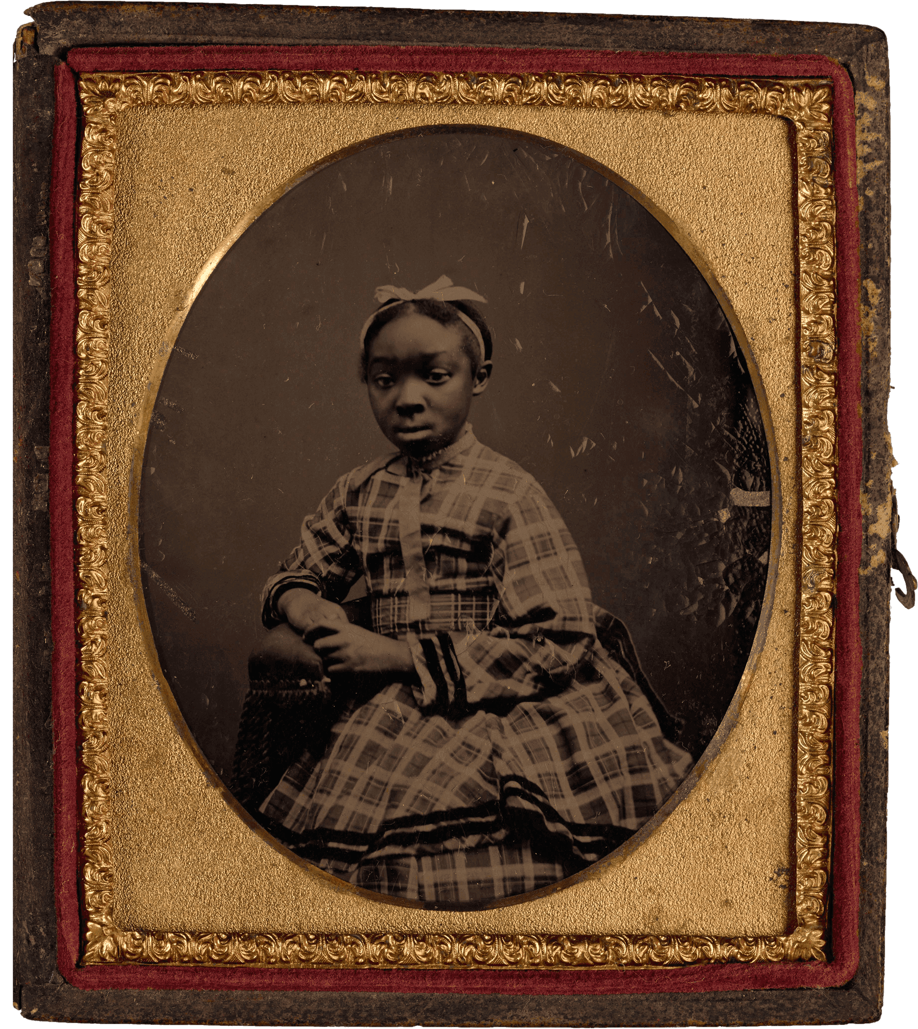 Portrait of a young girl in a plaid dress, seated and framed in an ornate gold-bordered case.