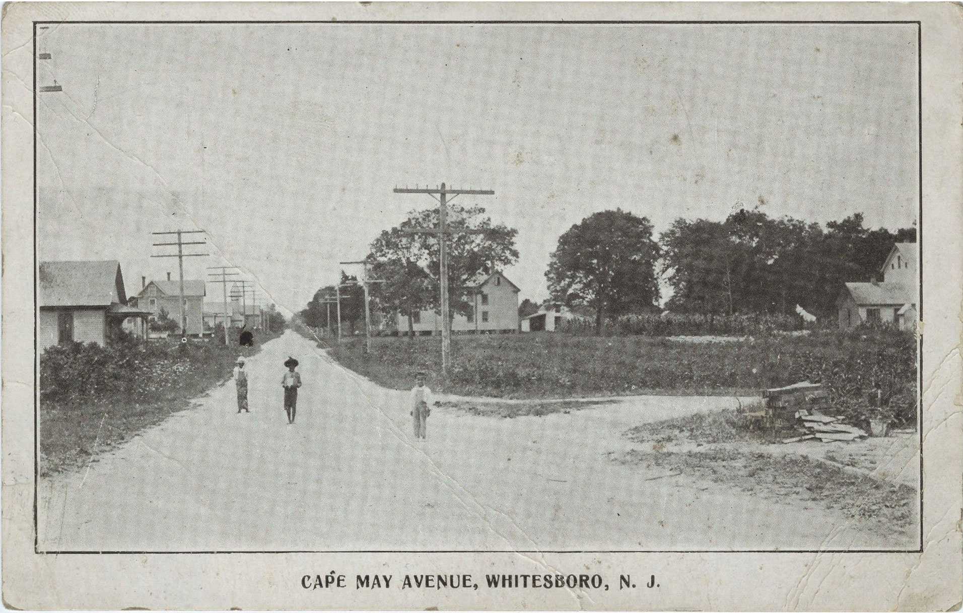 Black and white photograph of three children walking down street.  There are houses in the background.