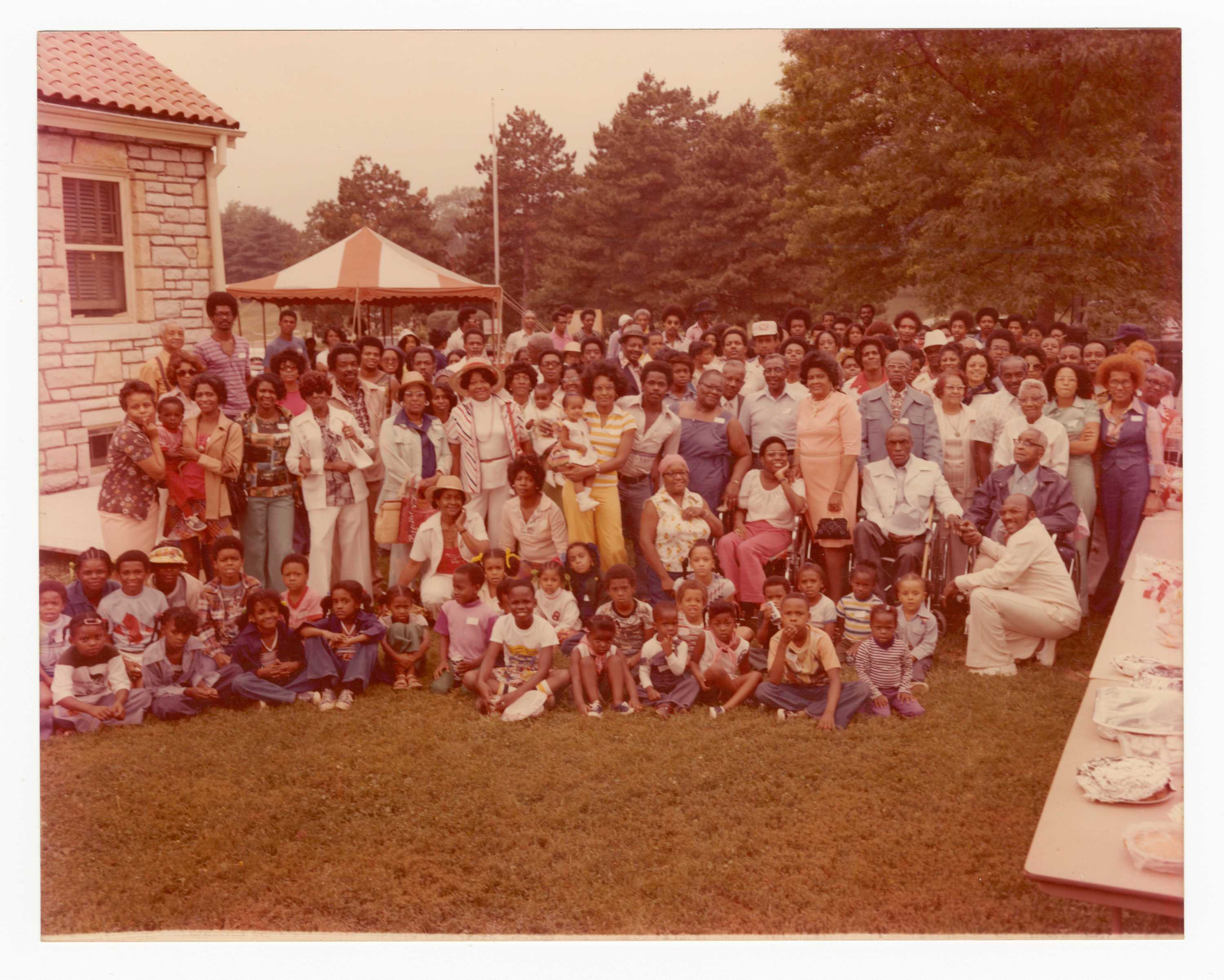 Color photograph of a large gathering of people outdoors. There are 7 rows of adults and 3 rows of children in front.