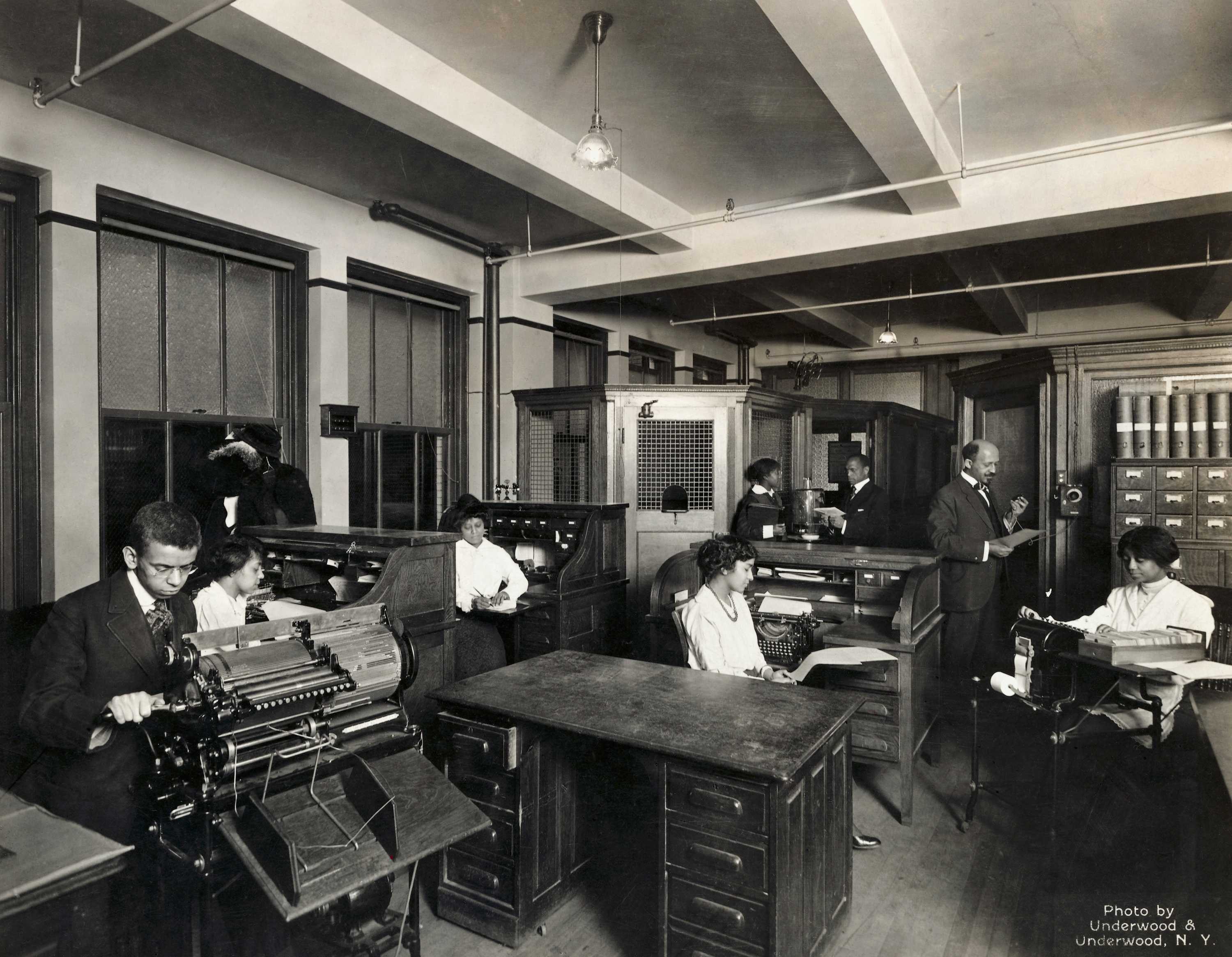 A black and white photo of W.E.B. Du Bois and others work at their desks with typewritters.