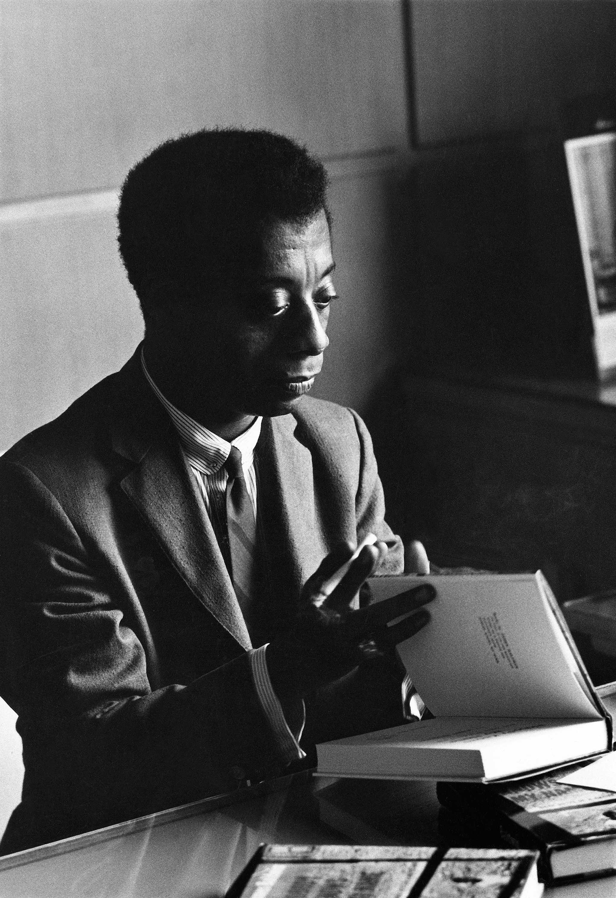 Black and white photograph of James Baldwin seated with a book in his hands