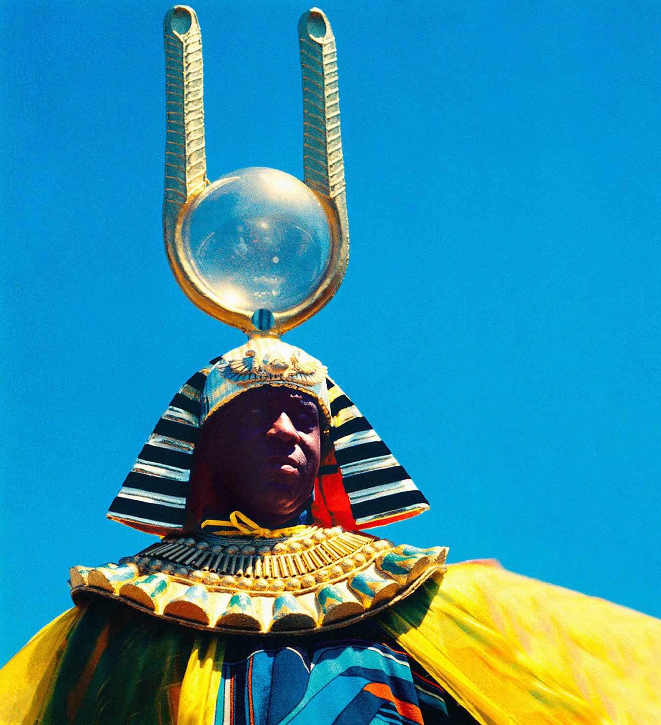 Sun Ra, a black alien , is dressed in a pharaoh looking headdress and colorful yellow costume.