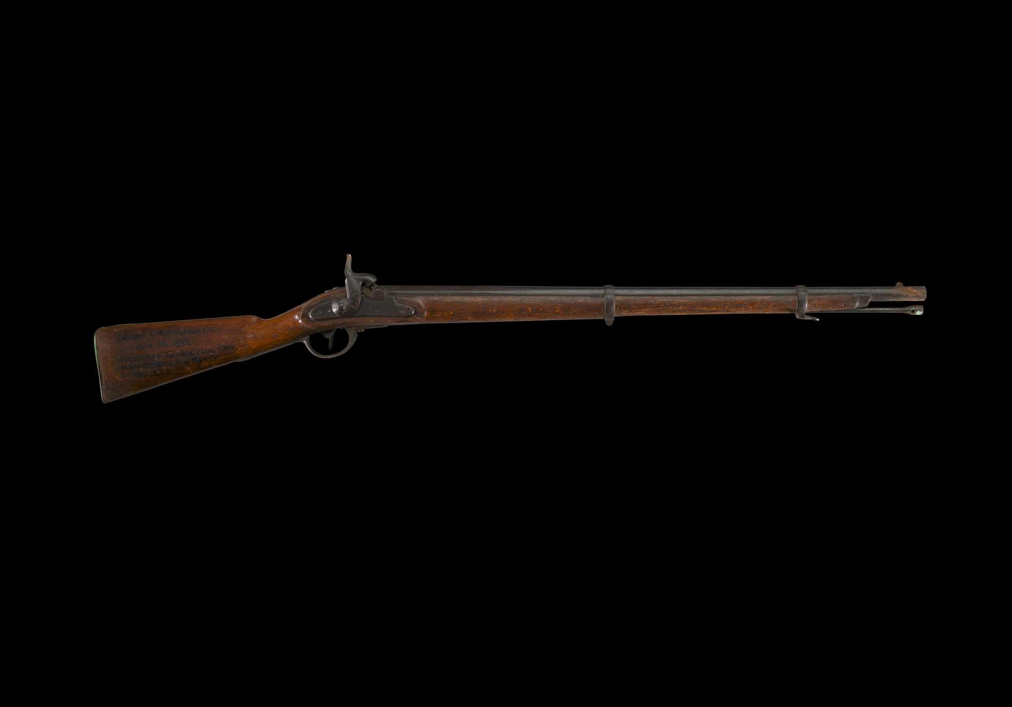 An Austrian Model 1854 .54 caliber Lorenz rifle constructed of primarily of a beech stock; steel barrel, breech ramrod; and brass butt plate and other fittings. The oxidized barrel features a front sight, stored ramrod, barrel bands, and shorted front stock. The proper left lock plate is missing. There are various markings throughout; the largest engraving was added post-manufacture and constitutes the entire proper right stock: [CAPTURED AT PORT HUDSON LA. / JUNE 13, 1863 / PRESENTED TO HON. ELIAS ROOT / BY THE OFFICERS AND MEN OF / 110 N.Y.V. Co I]. The proper right lock plate, parallel to the hammer, shows an engraving “860”. A “26” is painted in a square on the proper left of the stock. There is a long split in the stock’s wood from the butt, and areas of wood replacement closest to the butt, where an oxidized plate features the engraving of “C S” below a stock screw. An off-white auction tag identifying the rifle and lot number, is tied by string to the trigger guard.