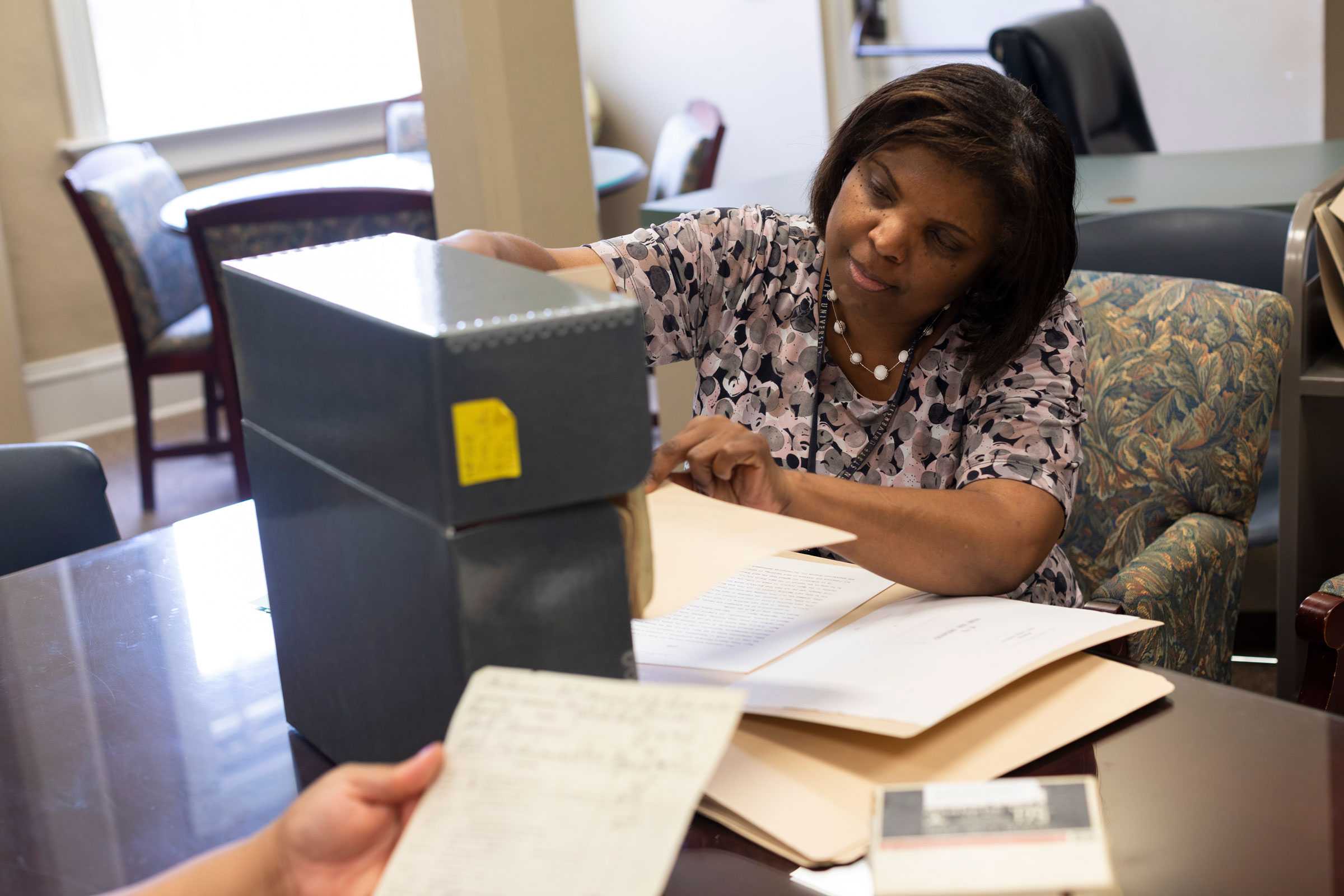 A woman examines documents from archival boxes on a desk in an office setting.