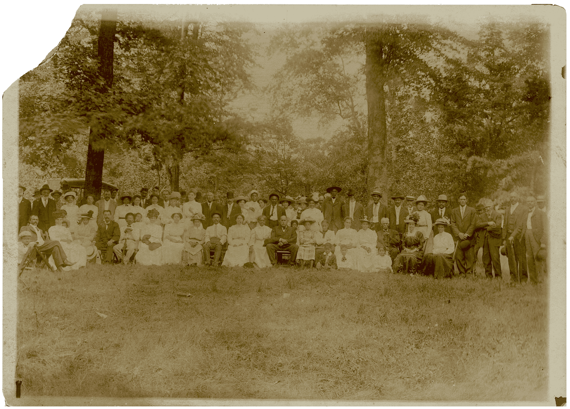 A sepia tone photograph of a family reunion. About 30 people are posed for the portrait in a wooden area.