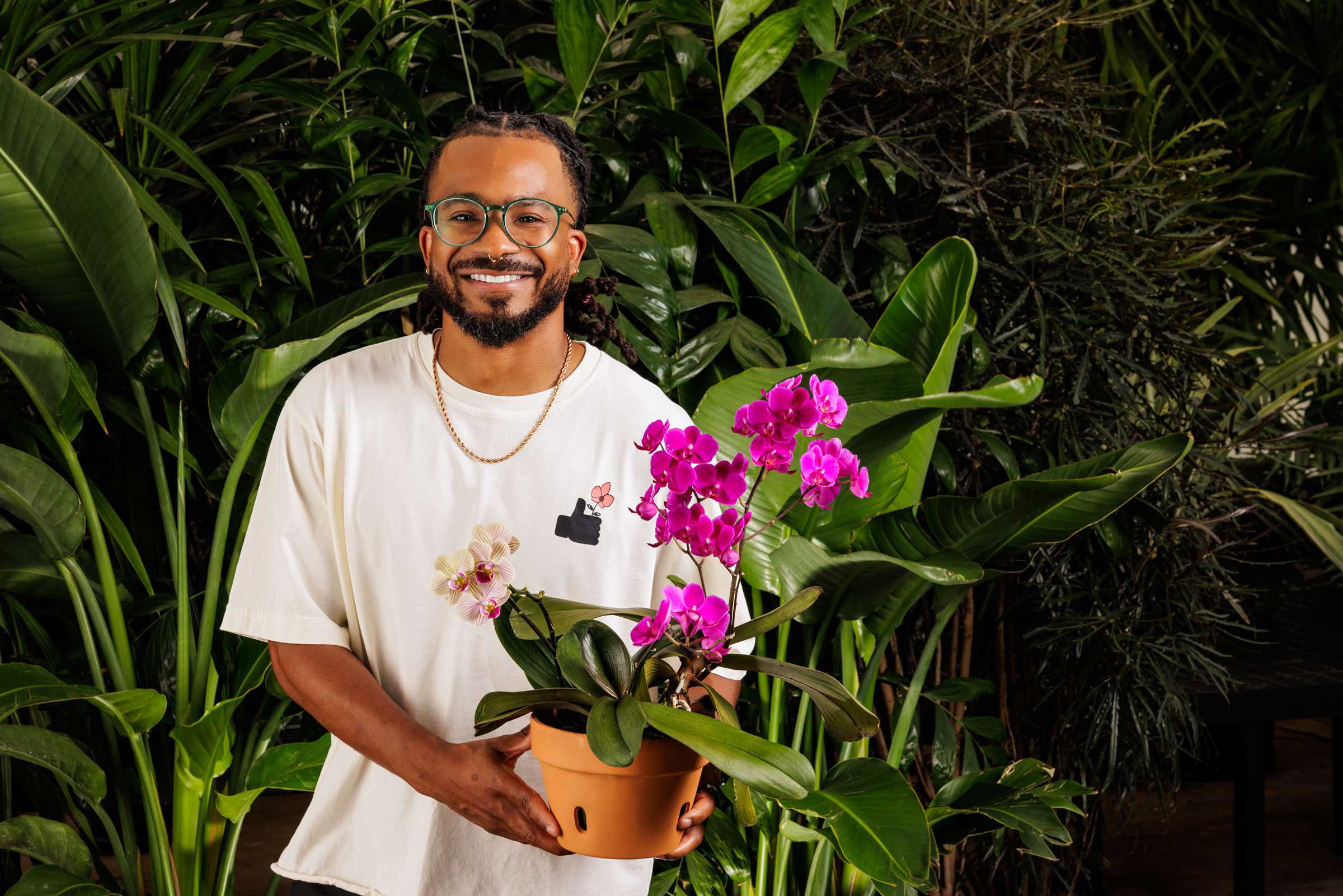 Person holding a pot with vibrant purple orchids, surrounded by lush green plants.