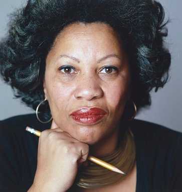 A colored photograph of Toni Morrison, looking directly at the camera. She is resting her chin on her fist, which is holding a pencil.