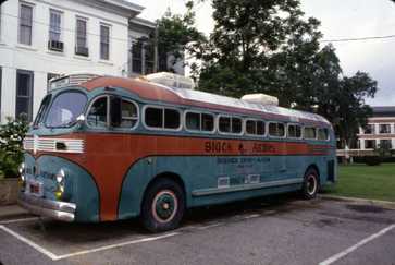 Vintage teal and orange bus parked in a lot, labeled “Black Archives Research Center & Museum,” with buildings and trees in the background.