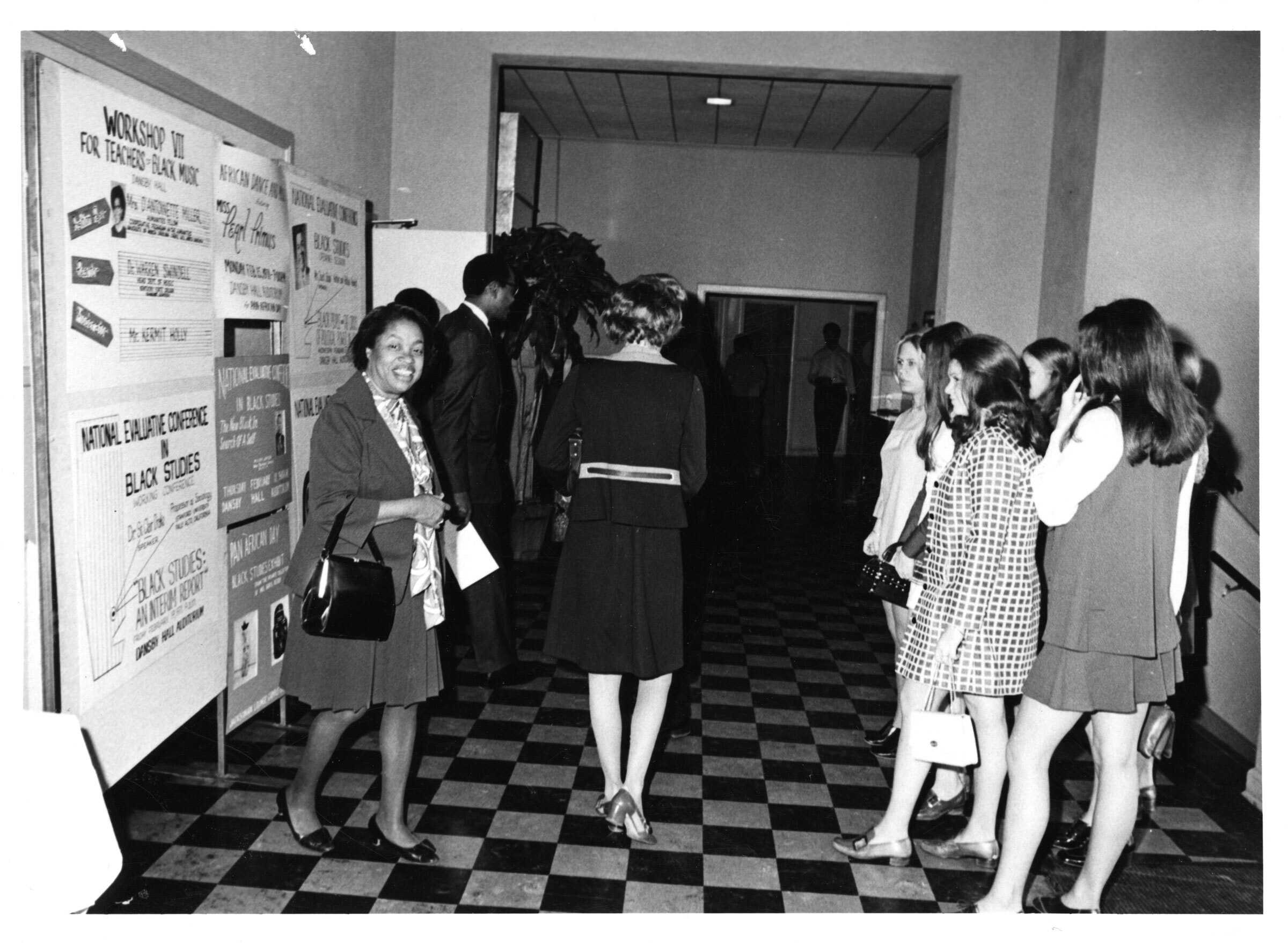 Group of people including author Margaret Walker, in a hallway near a display board reading 'Workshop for Teachers of Black Youth' and 'National Equalize Conference Black Studies.'