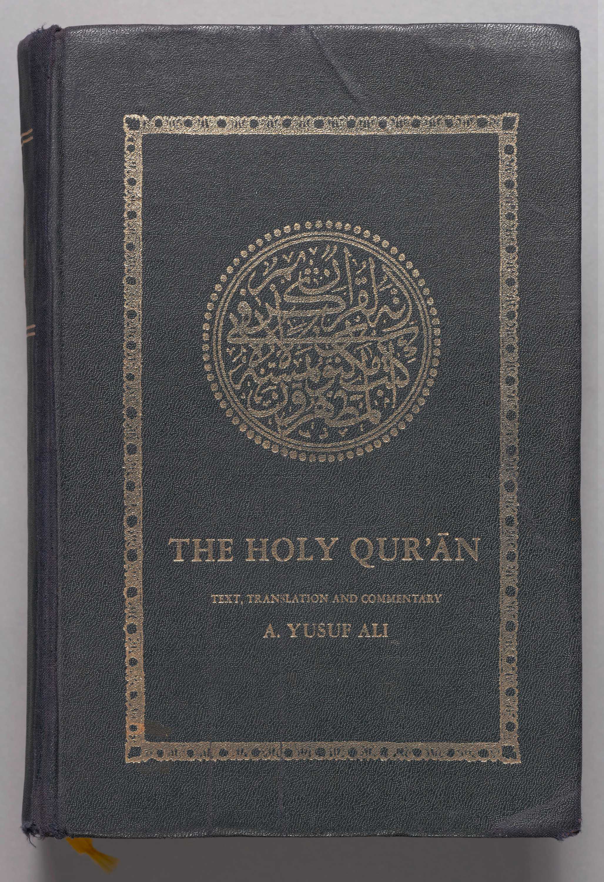 This Qur'an is a thick hard-backed book with a black cloth cover imprinted with gold inked letters and designs.