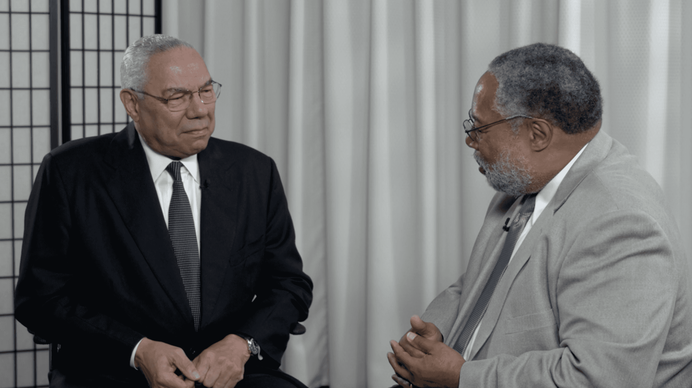 A photograph of Lonnie Bunch interviewing Colin Powell. Both men are dressed in suits, sitting and talking..