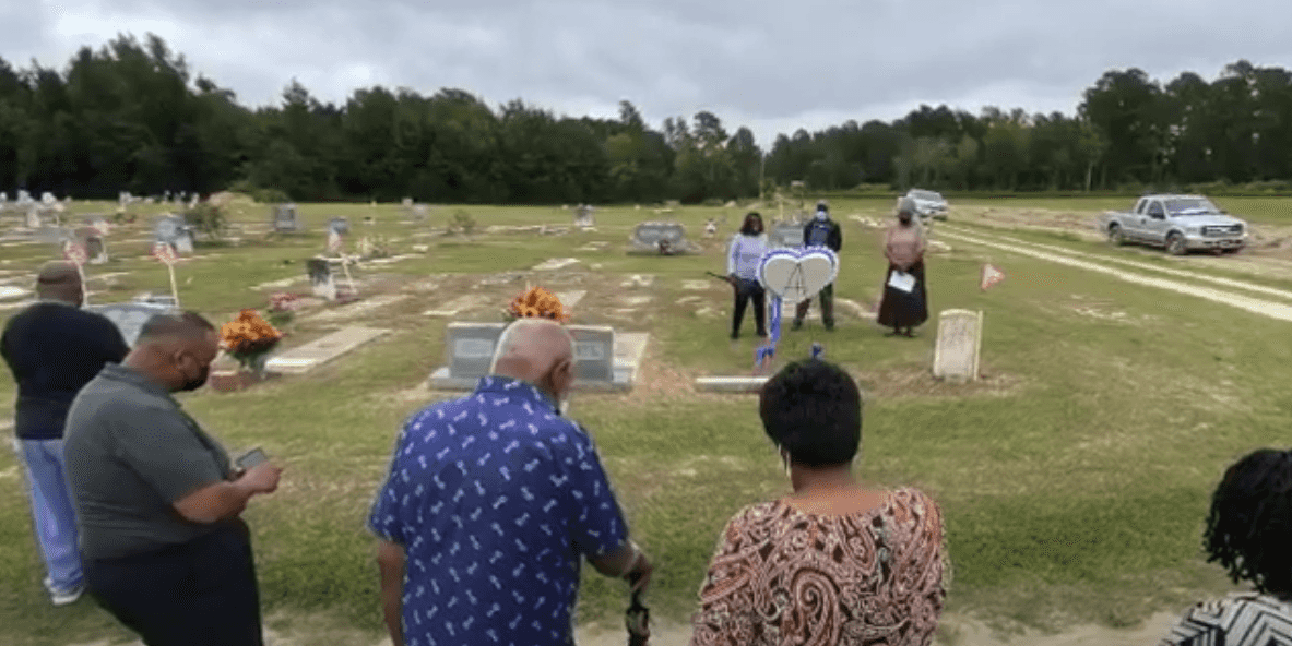 A still image from video about Millie Christine's family of various people standing in a cementary.