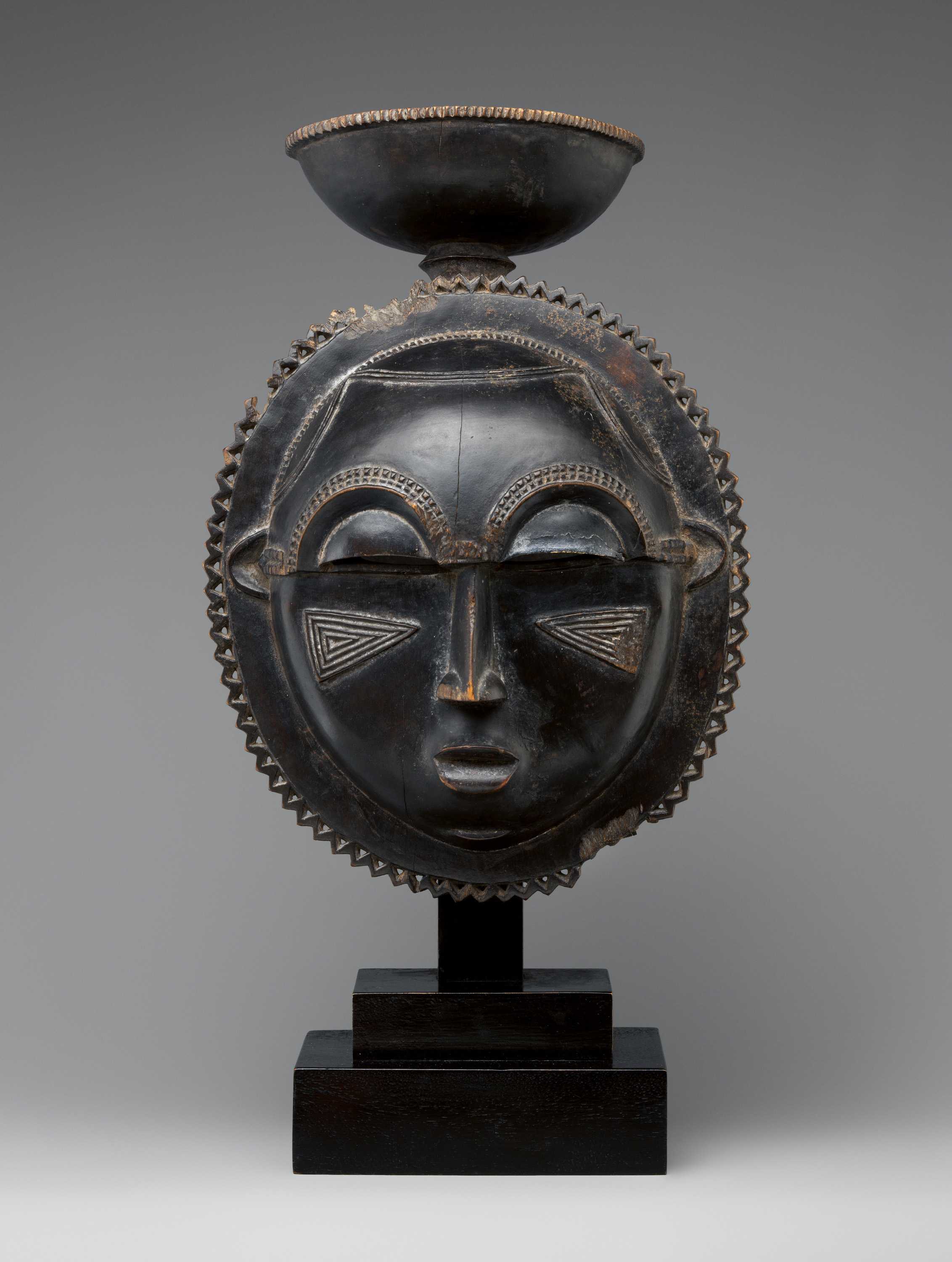 A dark colored moon statue sits on a plain backdrop. The moon has a face and structural design elements.