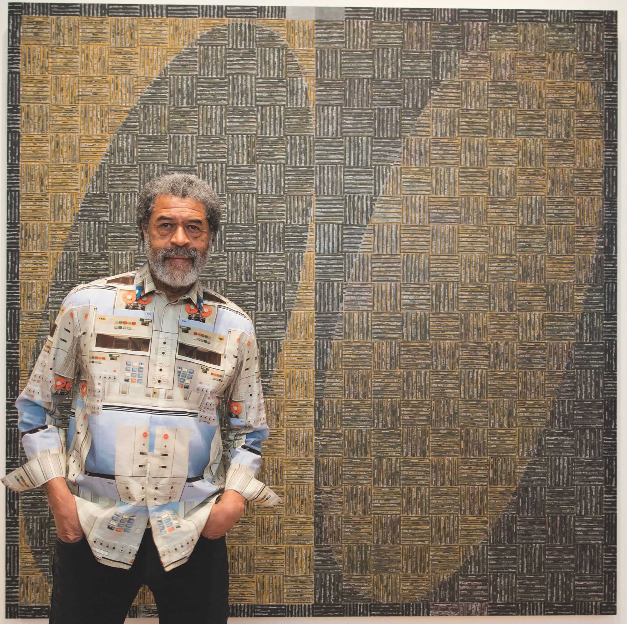 Man standing in front of a geometric-patterned artwork, wearing a shirt with a similar design theme.