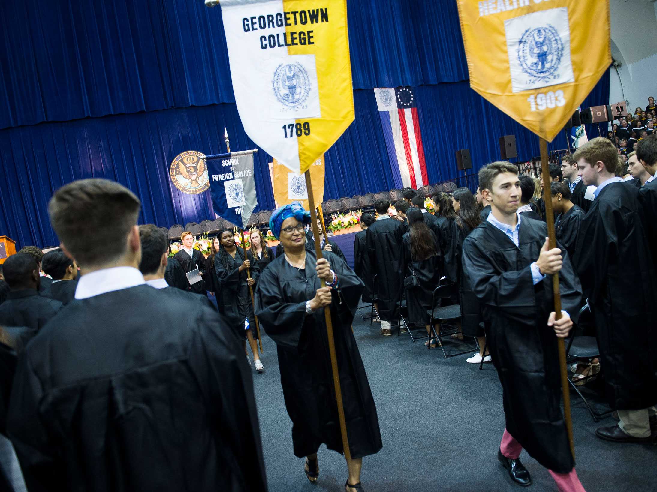 A woman is walking through the convocation holding the sign that says 'Georgetown College, 1879."