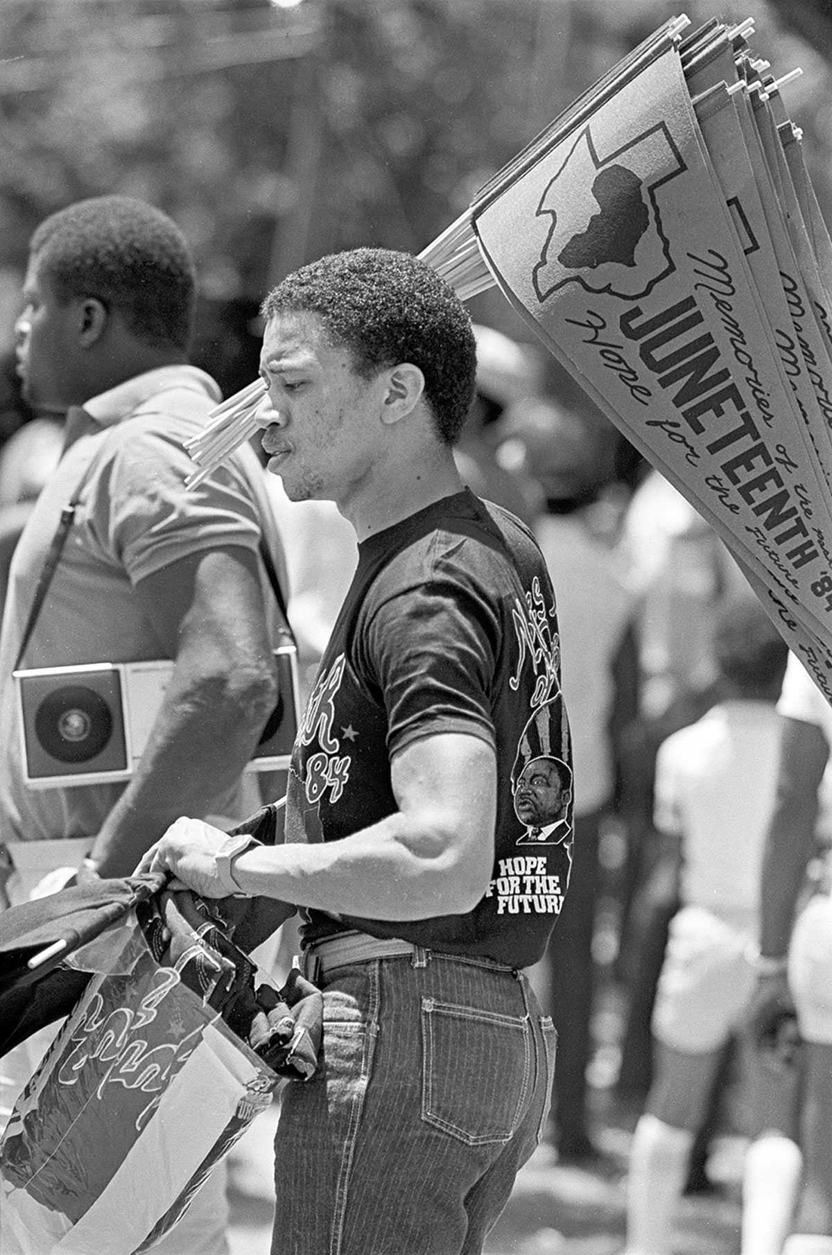 Black-and-white photo of people at a Juneteenth event, one holding a fan with "Juneteenth" printed on it.