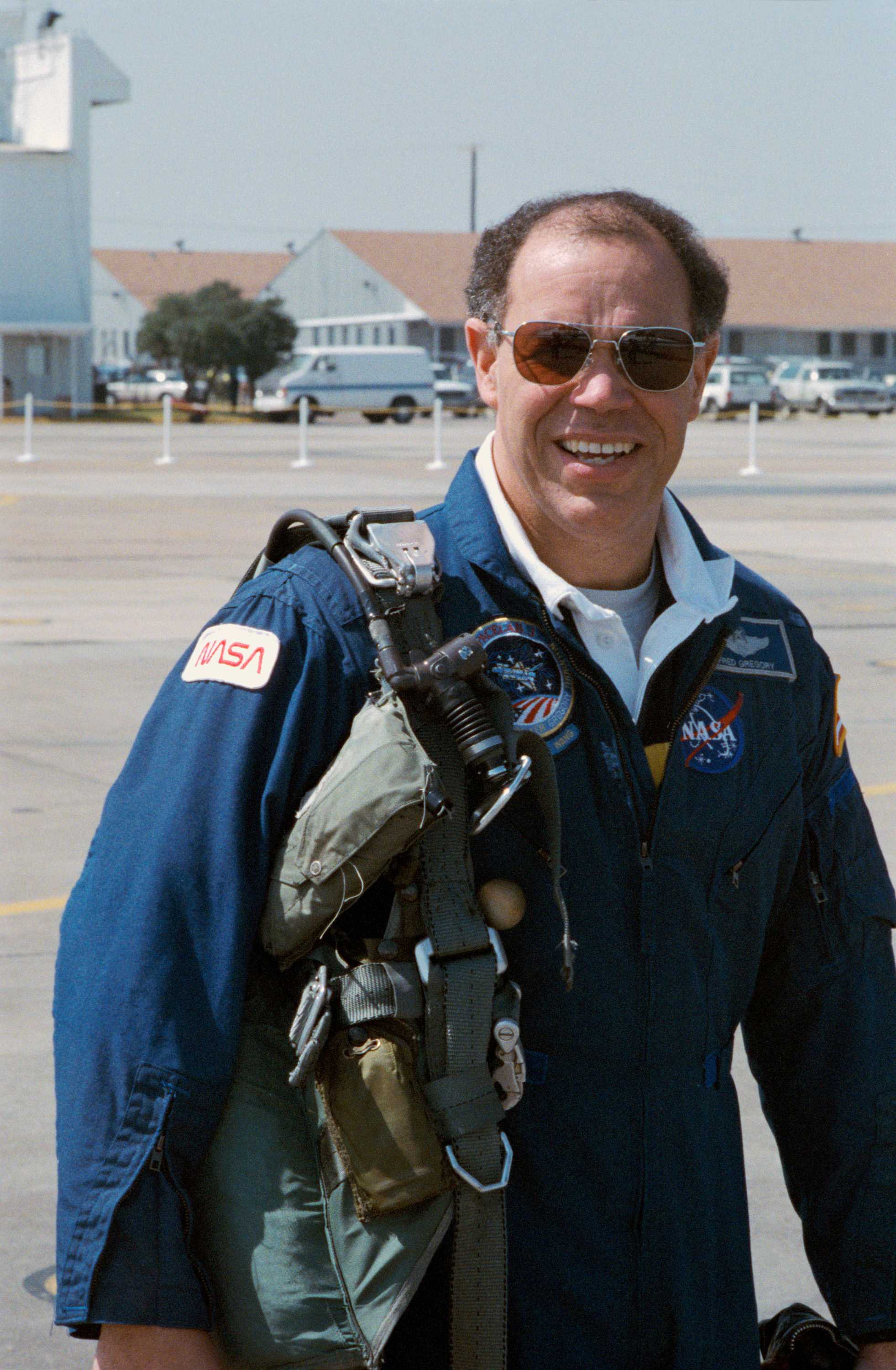 Gregory is dressed in a blue NASA suit with flight gear laying over his left shoulder, posing for a picture.